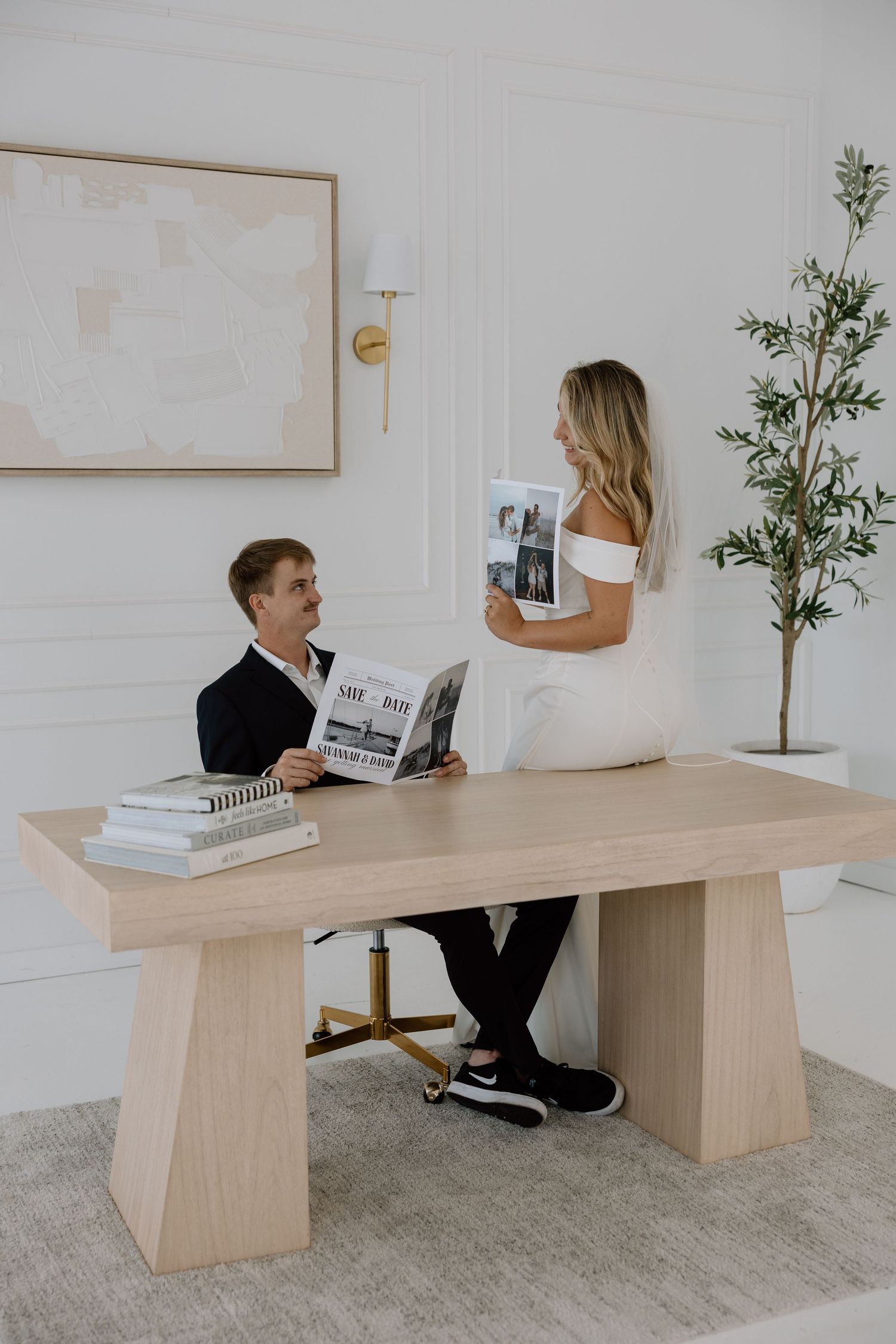 A couple plays around a long wooden table in a minimalist white room.