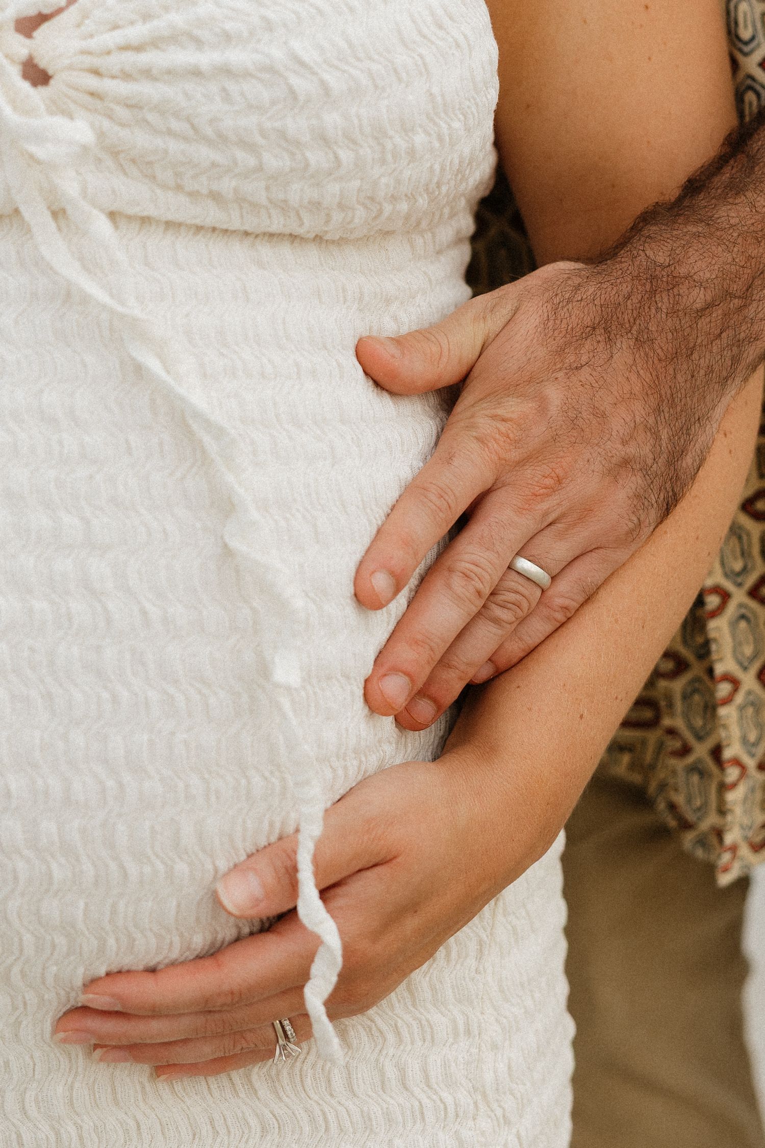 Close-up of hands tenderly touching white textured fabric of a dress.