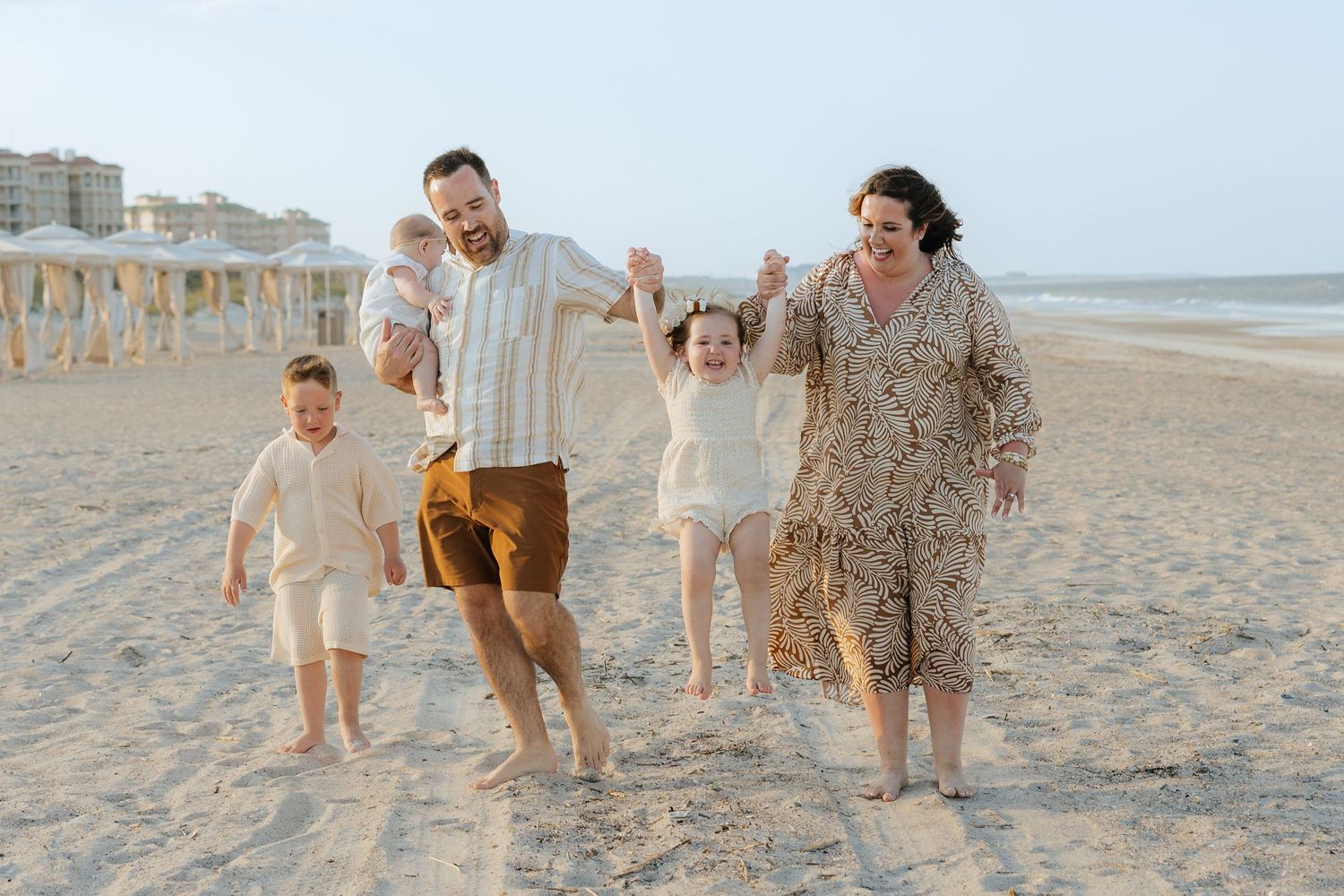 A joyful family runs together along a sandy beach at sunset with beach cabanas in the background at Omni Amelia Island Resort & Spa.