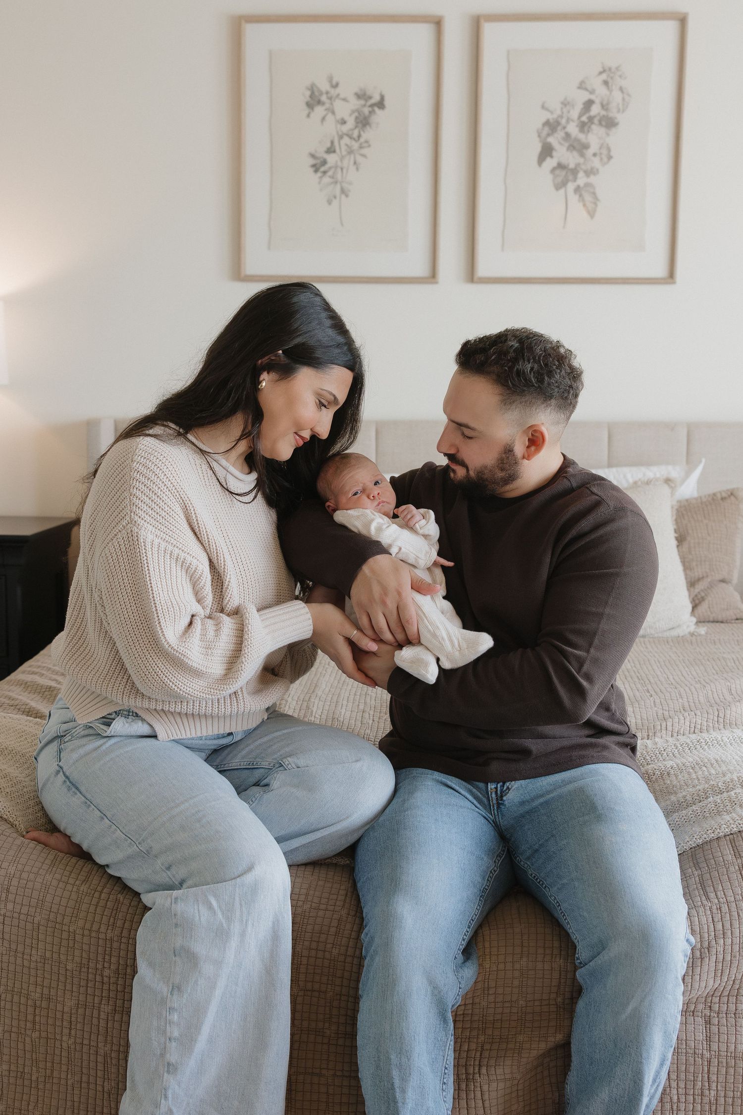 A couple sits together on a couch sharing tender moments with their newborn baby in a series of intimate photos.