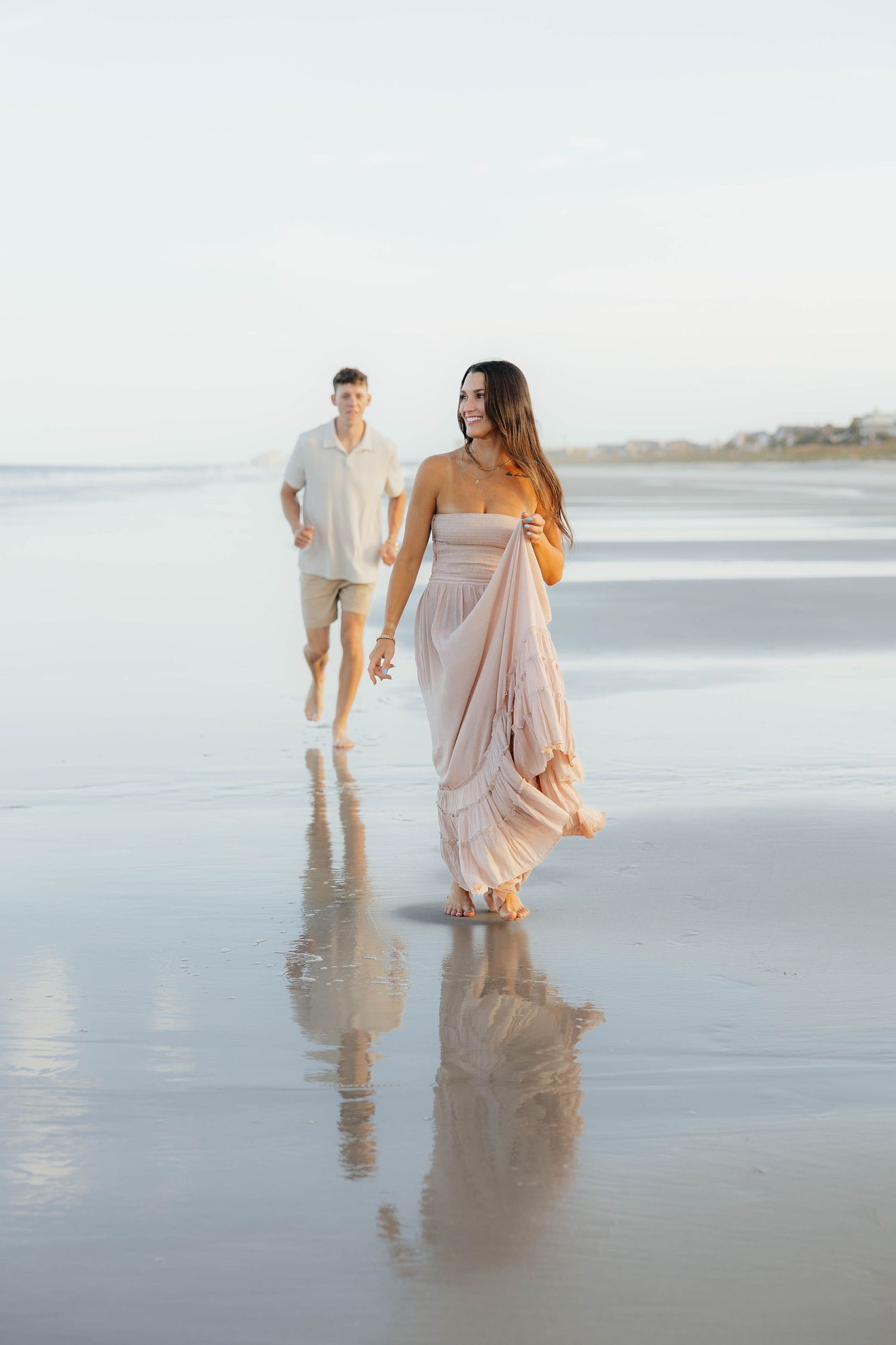 Couple walking and playing together on a serene beach at sunset with reflections in the wet sand.