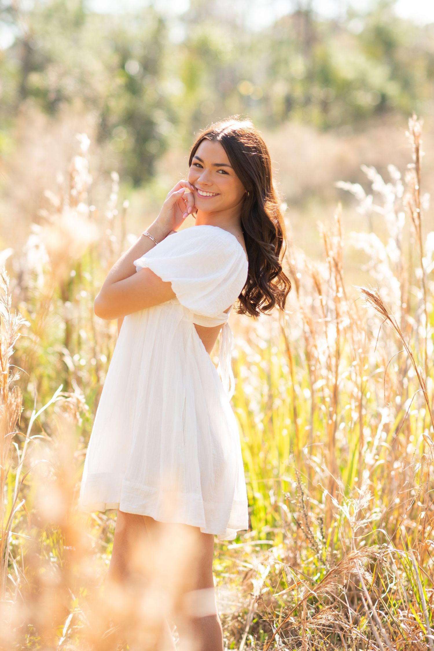 Young woman in white dress smiling in golden field of tall grass on sunny day.
