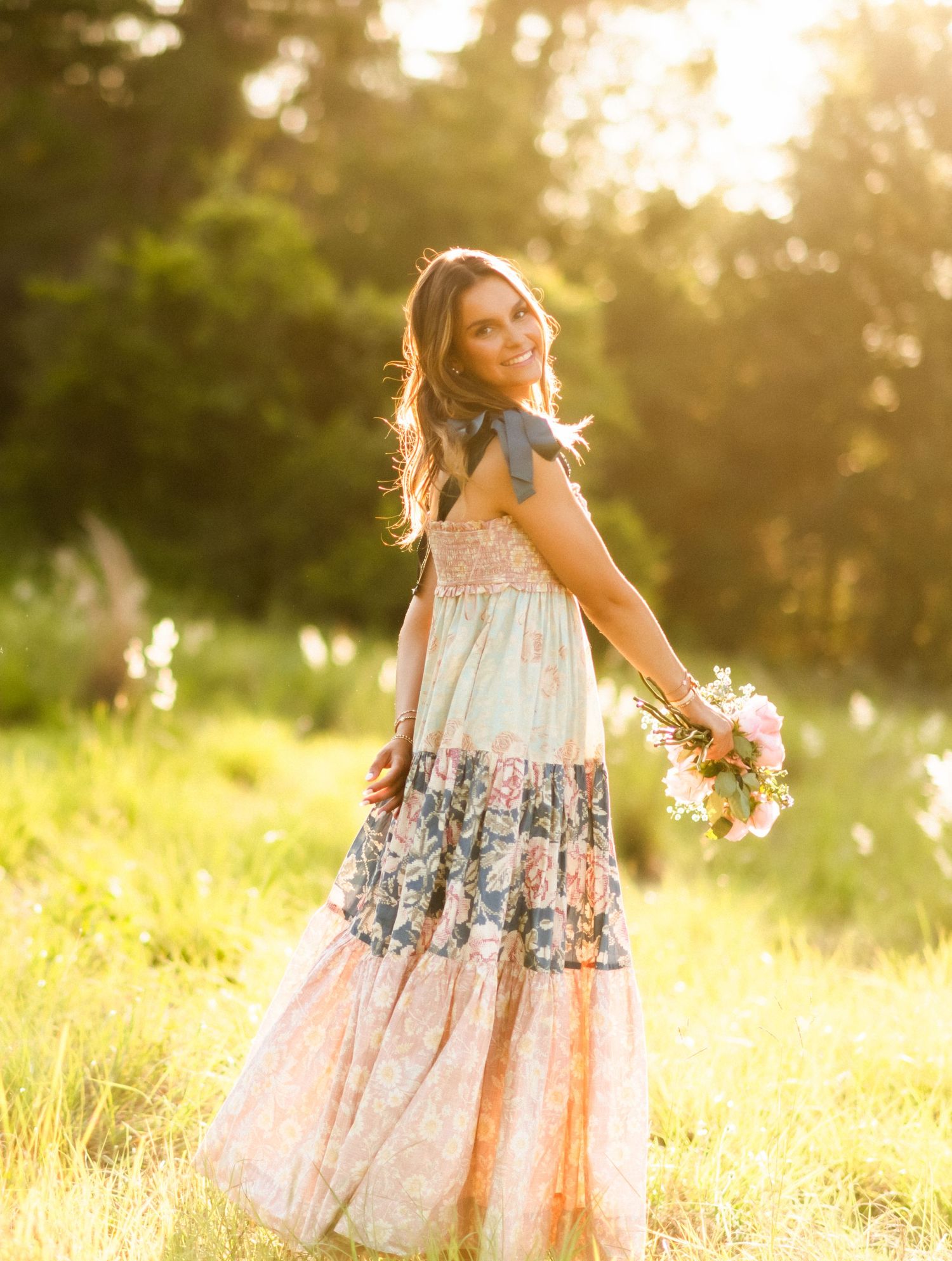 Woman in floral boho maxi dress holding bouquet in golden hour sunlight outdoors.