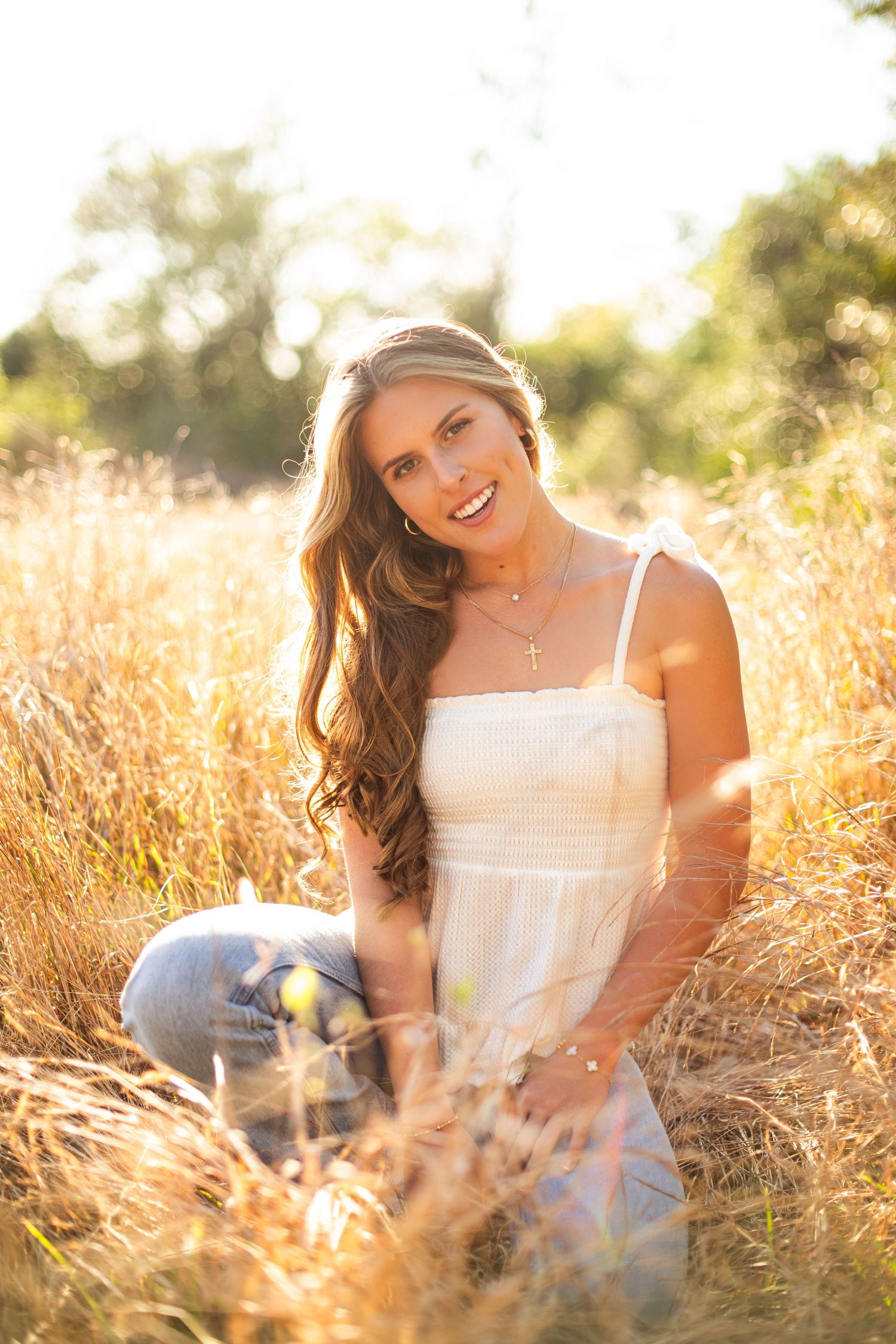 Person in white sundress sits in golden sunlit field of tall grass during sunset golden hour.