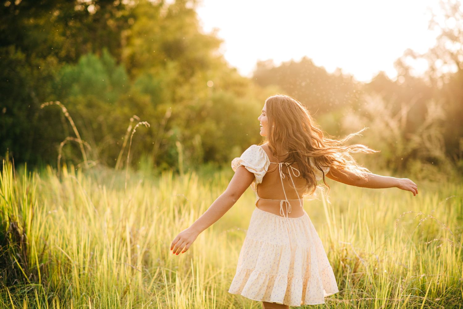 Woman in white dress spins joyfully in sunlit meadow at golden hour.