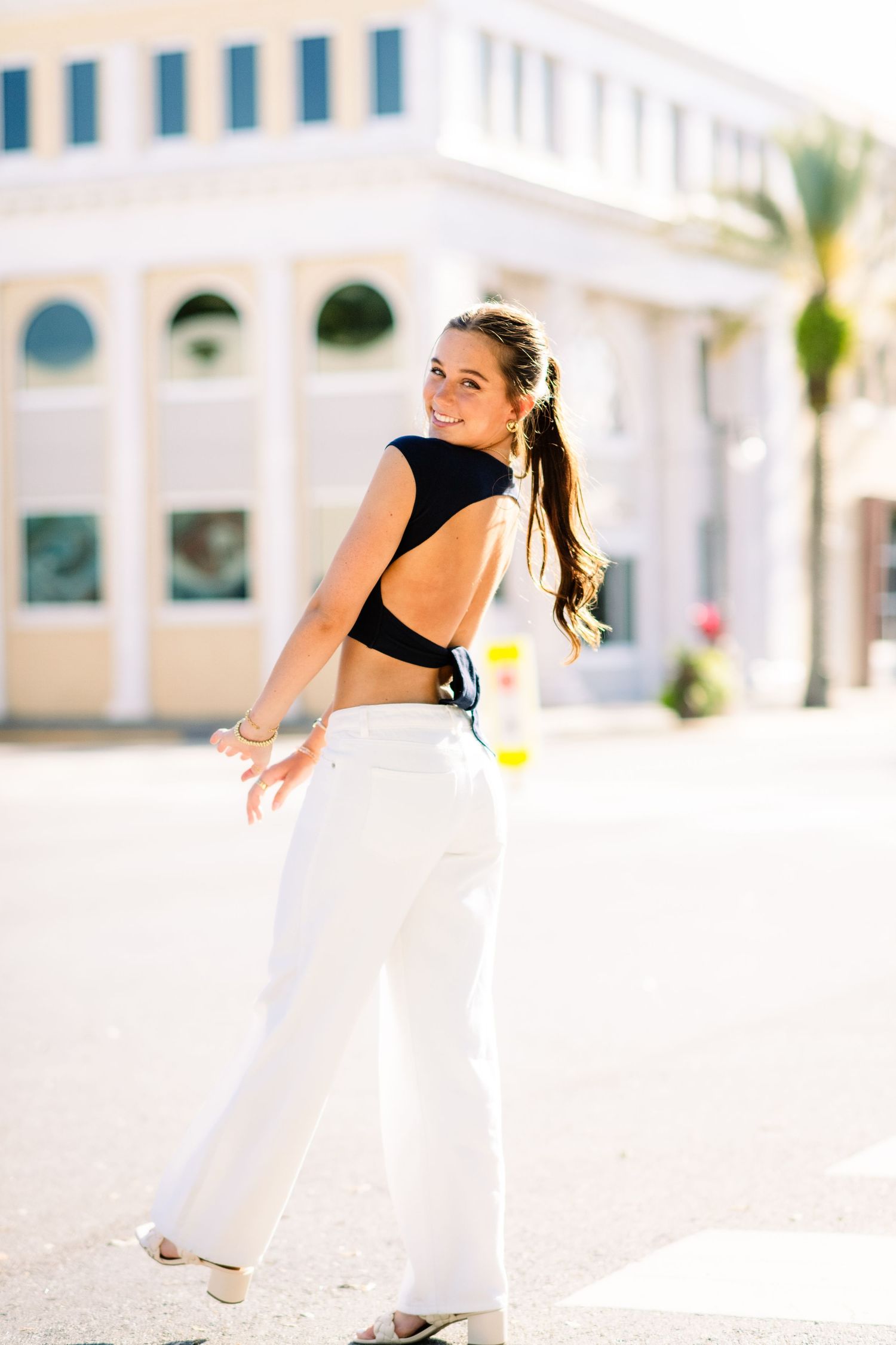 A figure jumps playfully in front of a white Mediterranean-style building with palm trees in the background.