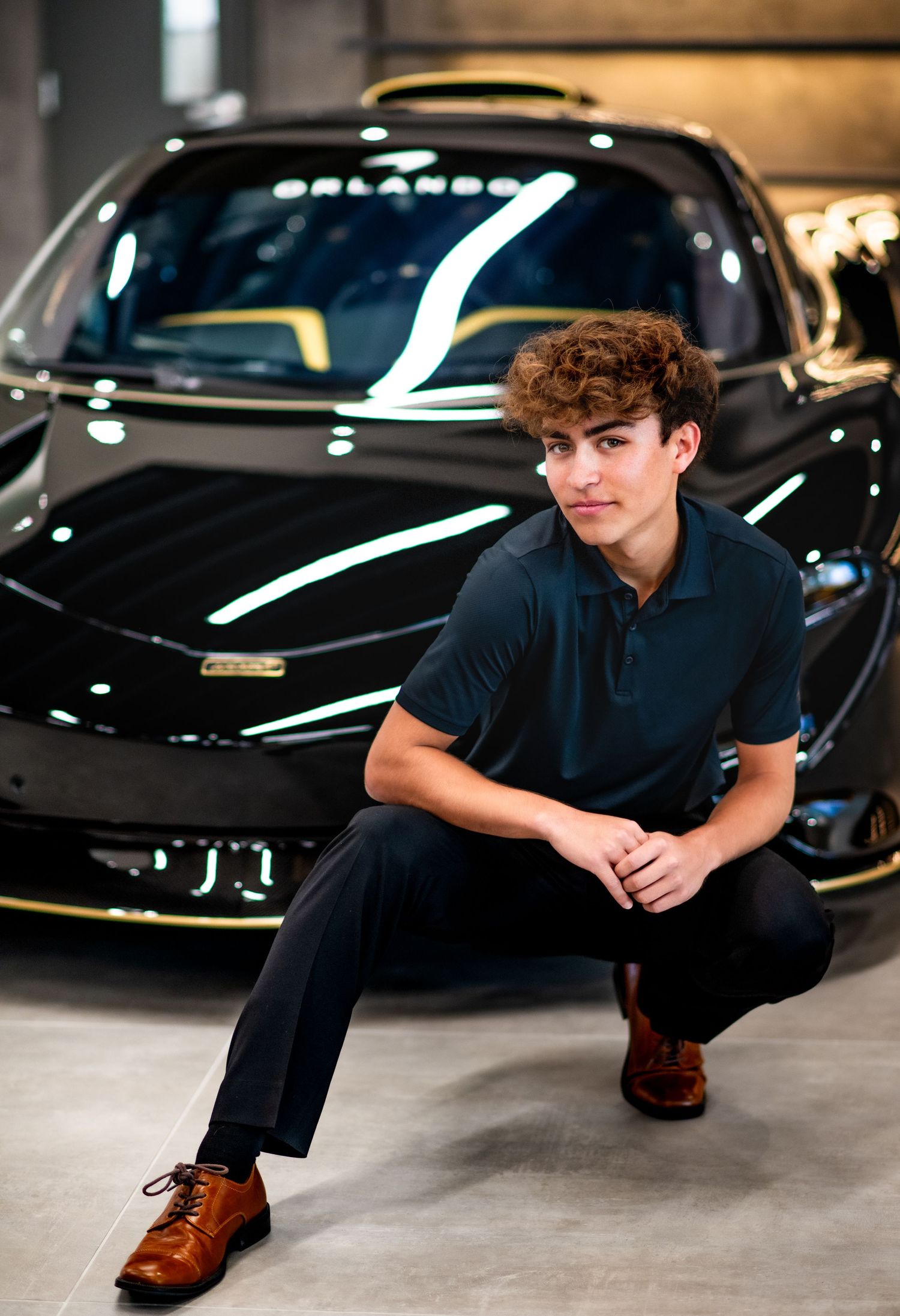 A person in dark clothing poses dramatically on the ground next to luxury cars in a dimly lit parking garage.