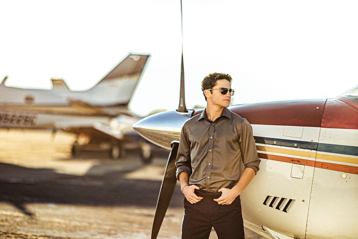 Casual portrait leaning against small aircraft propeller at airport.