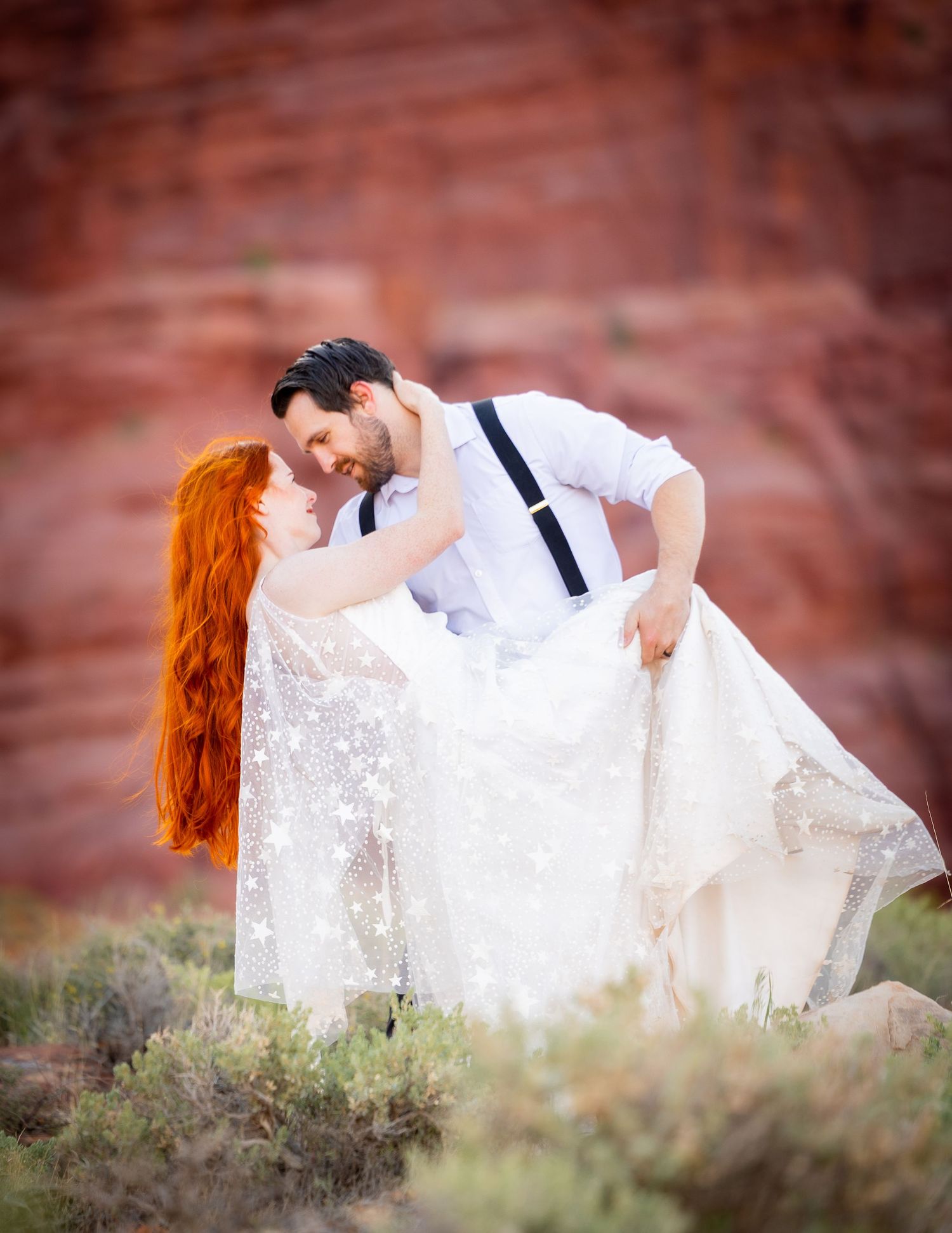 A romantic wedding couple poses in front of red rock formations during a desert photoshoot.