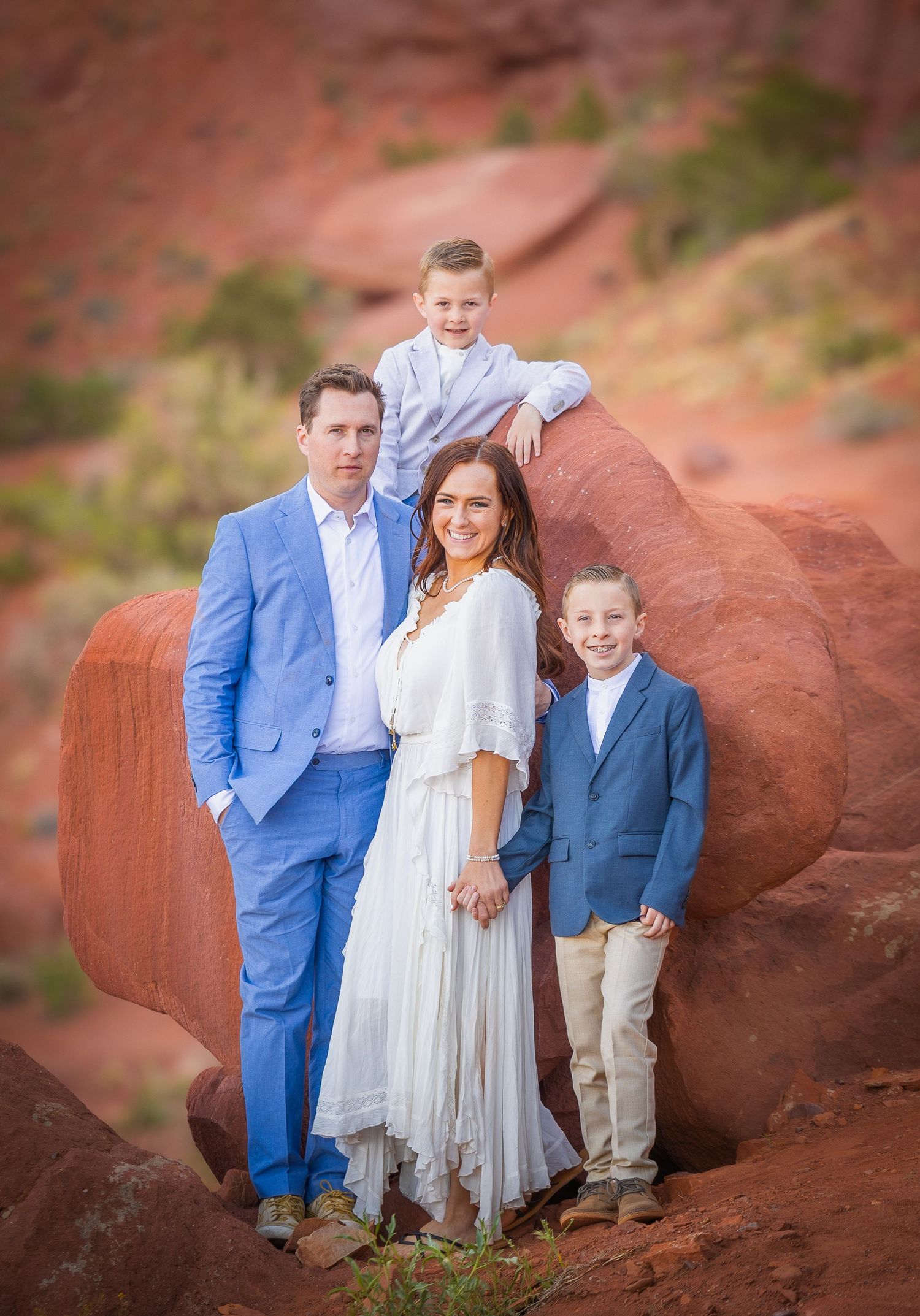 A family portrait session on red rock formations wearing coordinated blue and white outfits.
