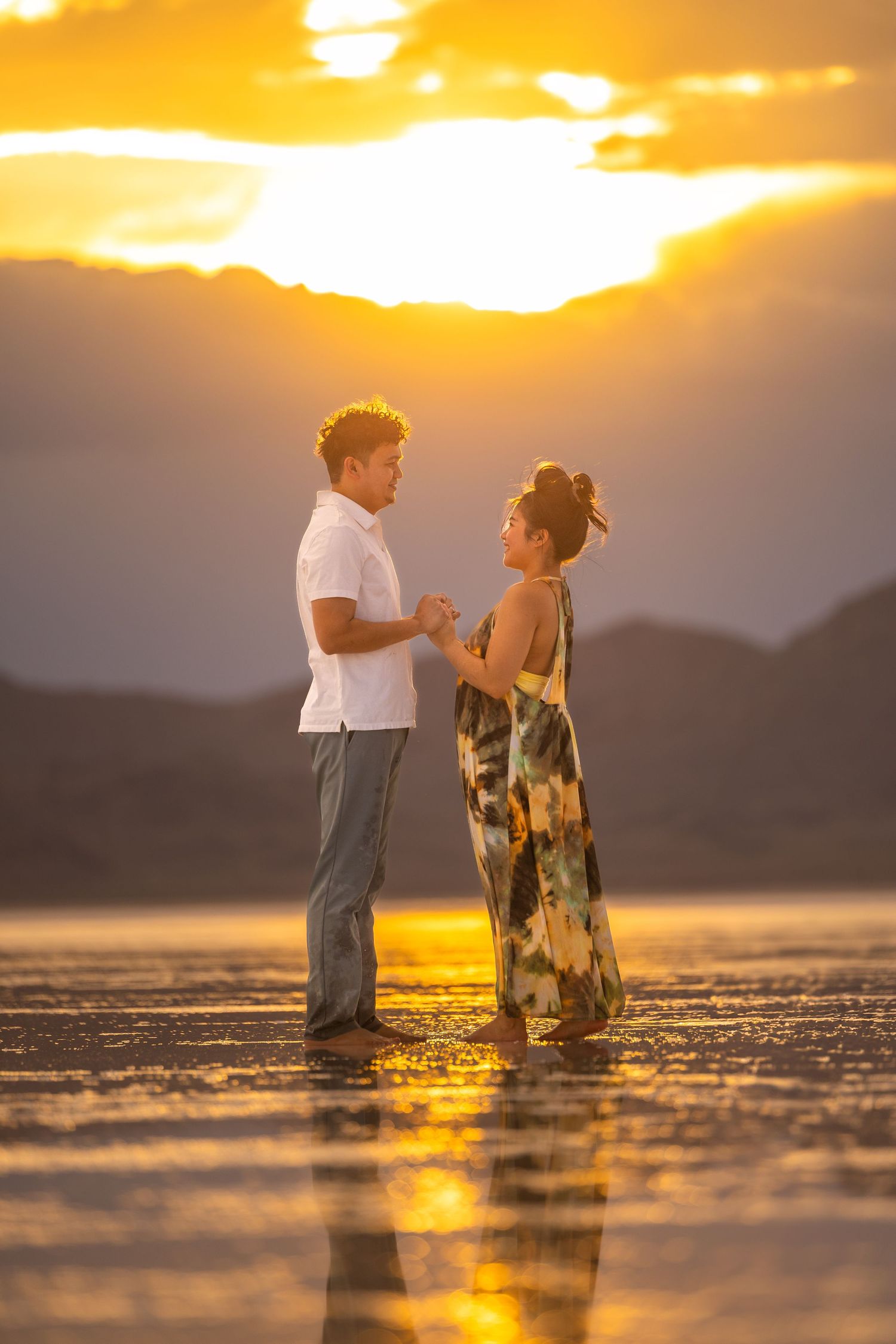 Couple having conversation at sunset on reflective surface with mountains in background.