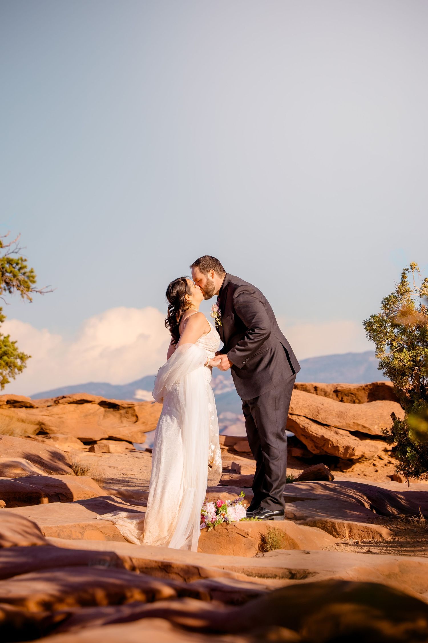 A wedding couple shares intimate moments on red rock formations at sunset.