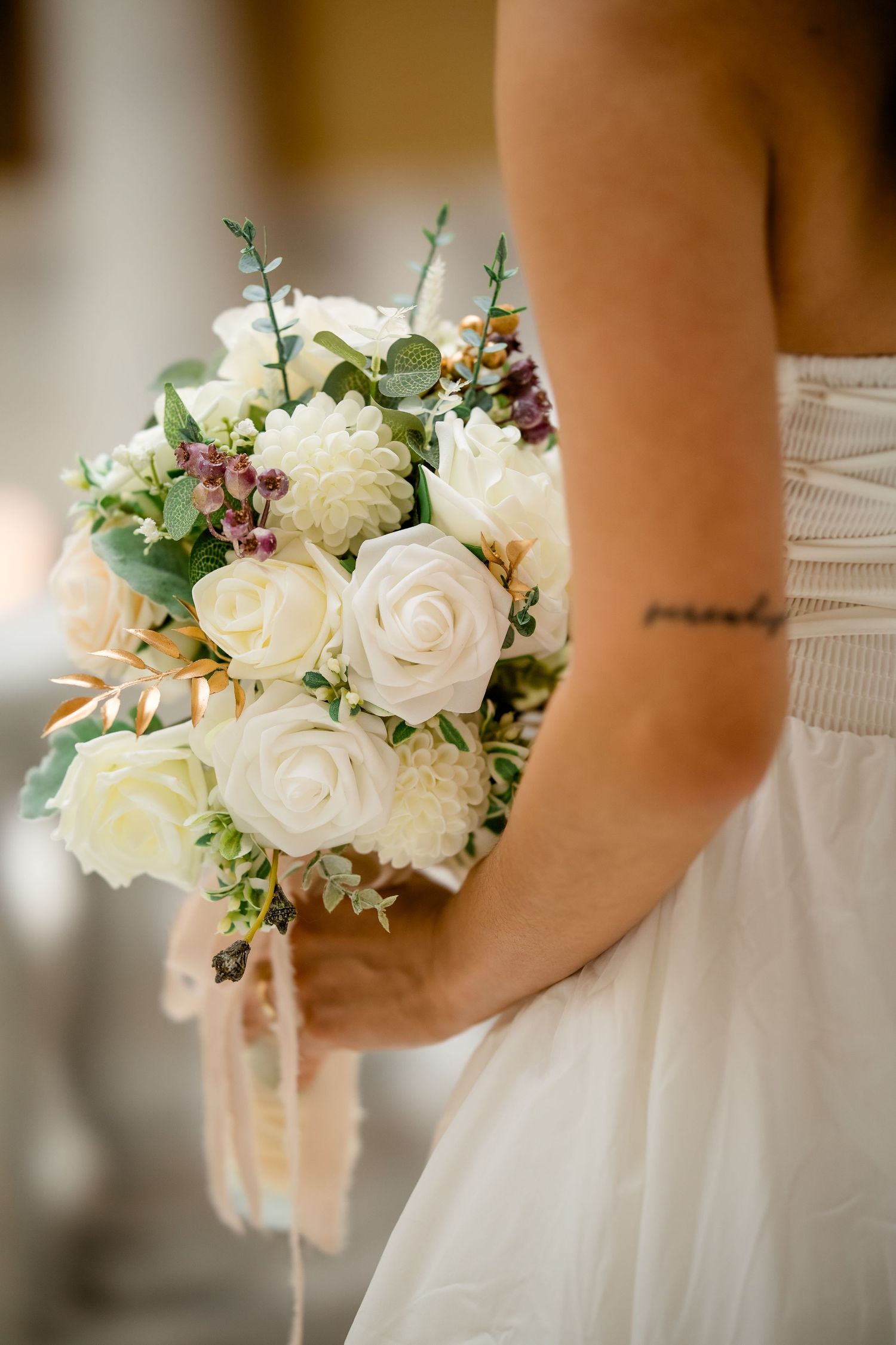 Close-up details of a white rose and eucalyptus wedding bouquet against a white dress.