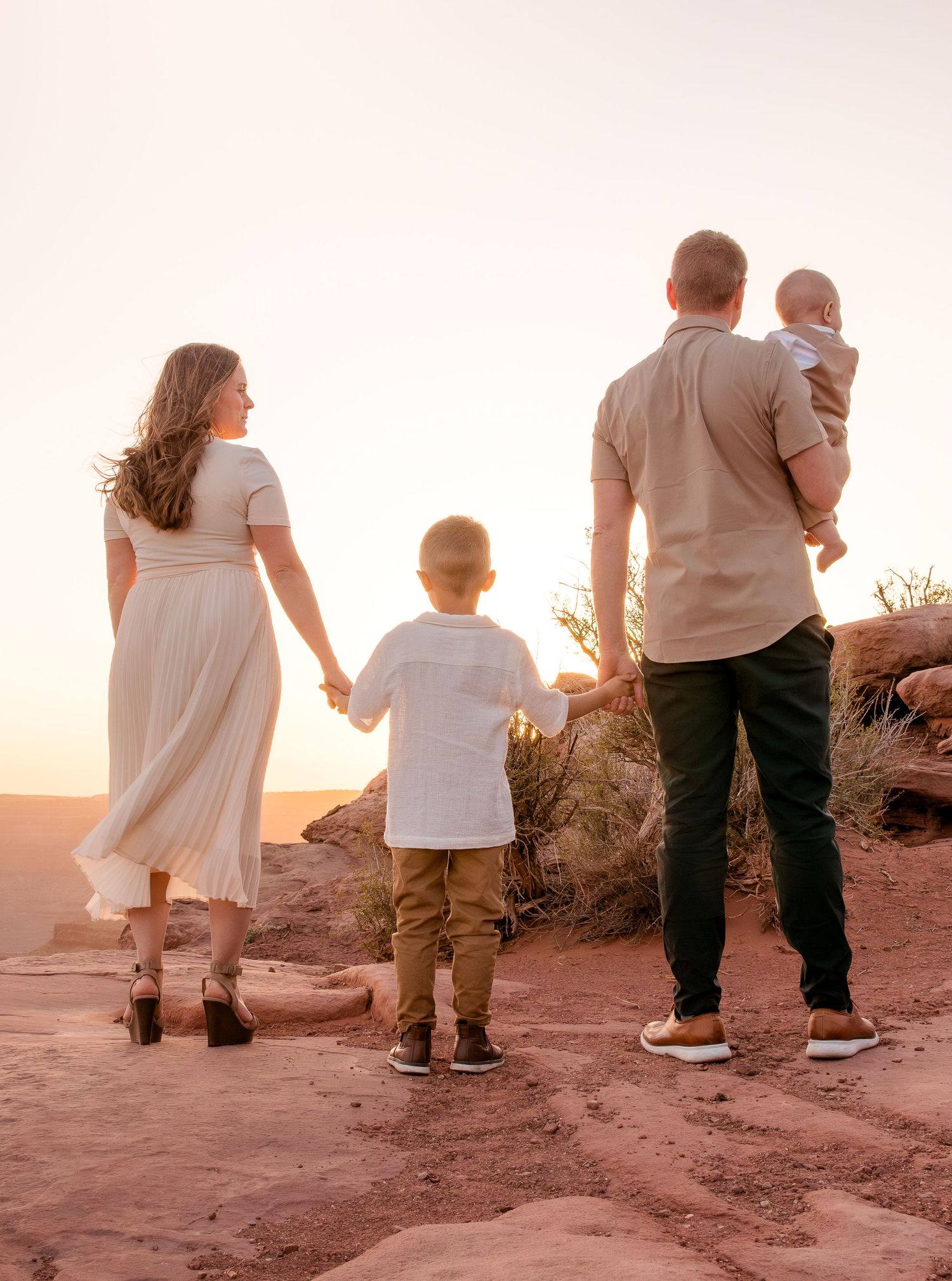 Family walking together on red rock formations during a desert sunset.