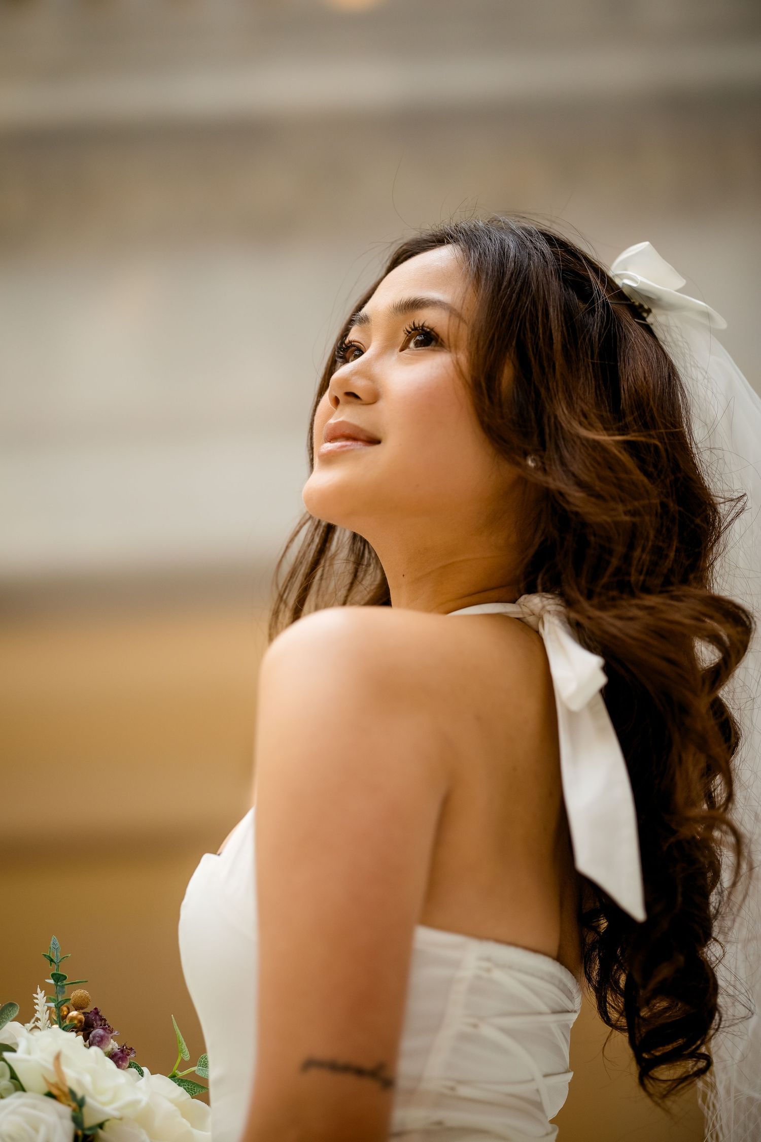 A bride in a strapless white wedding dress with dark curled hair looks upward in a romantic portrait series.