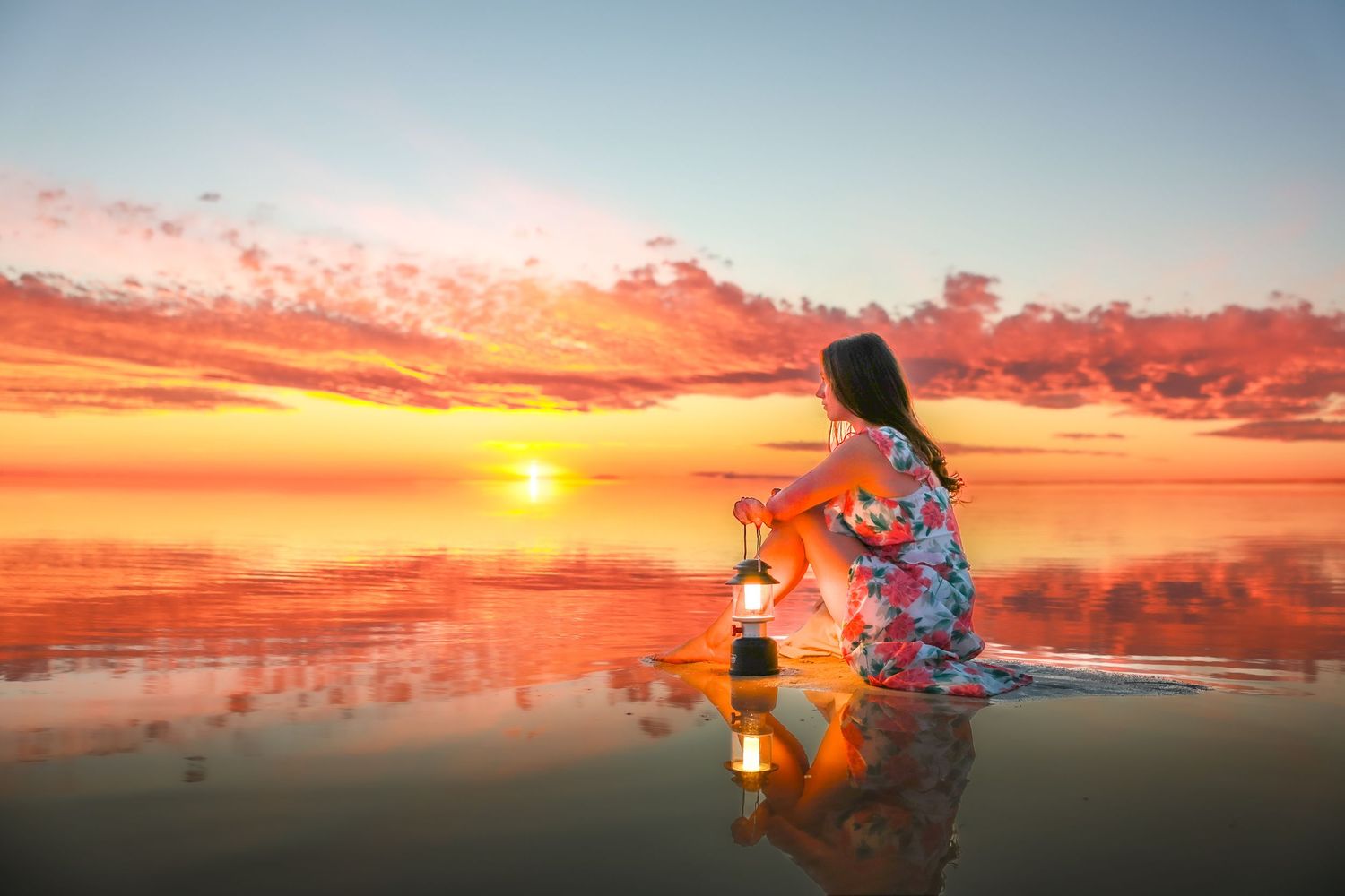 Person watching sunset while sitting on reflective water surface in colorful attire.