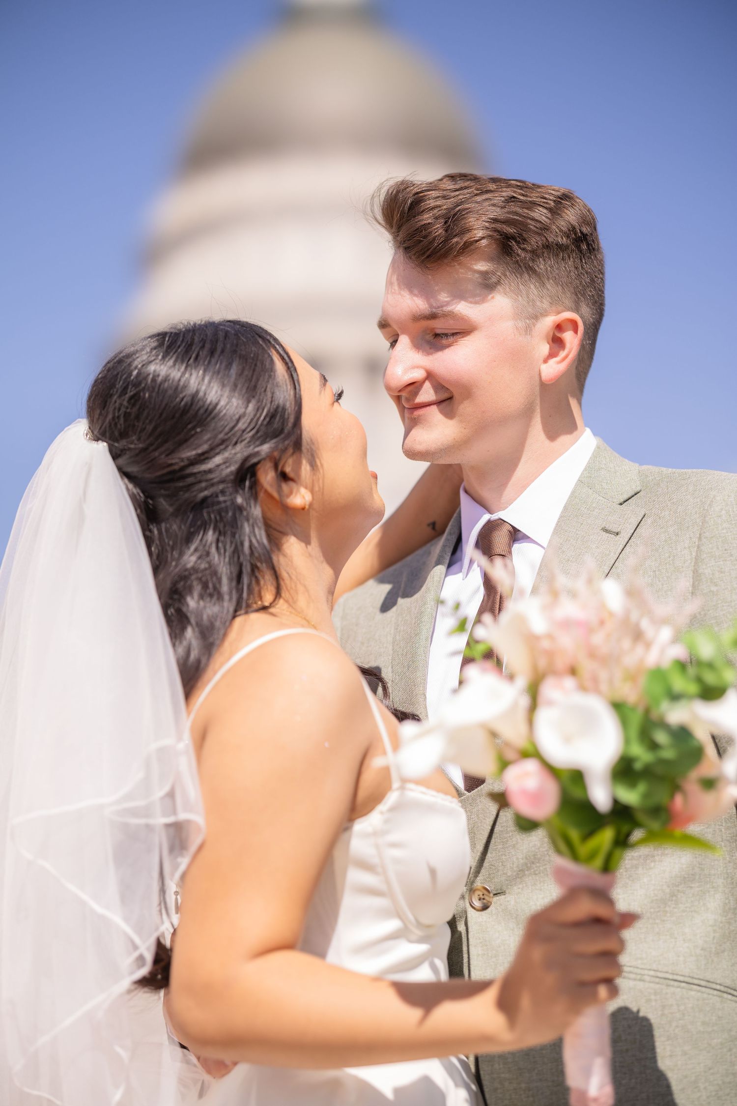 Romantic wedding moment captured against bright blue sky with soft natural lighting.