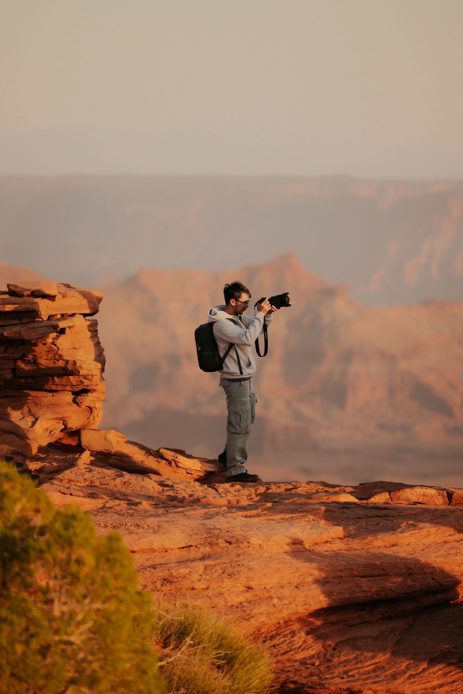 Photographer captures desert landscape from rocky outcrop during golden hour.