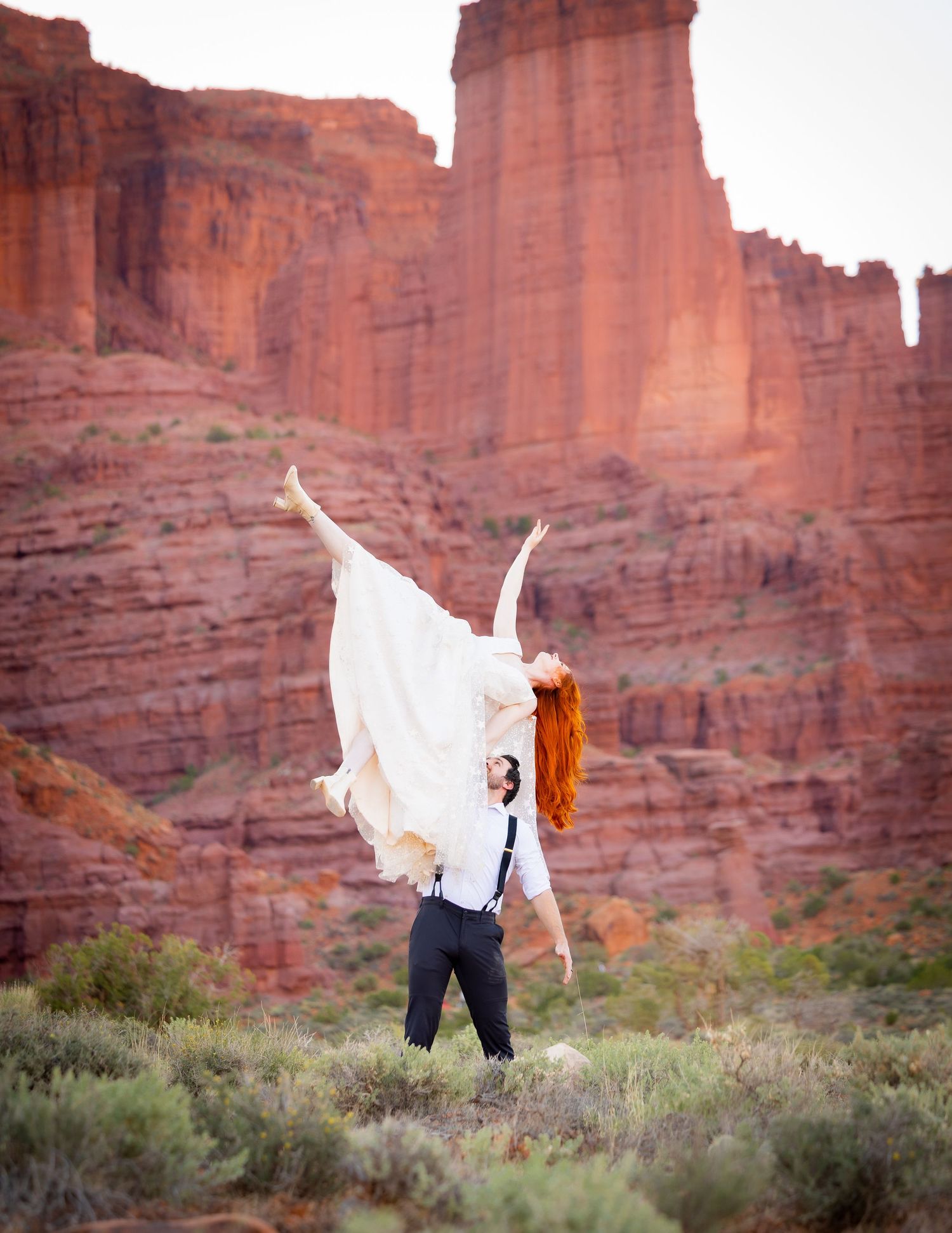 White dress flows dramatically against red rock canyon walls in desert landscape.