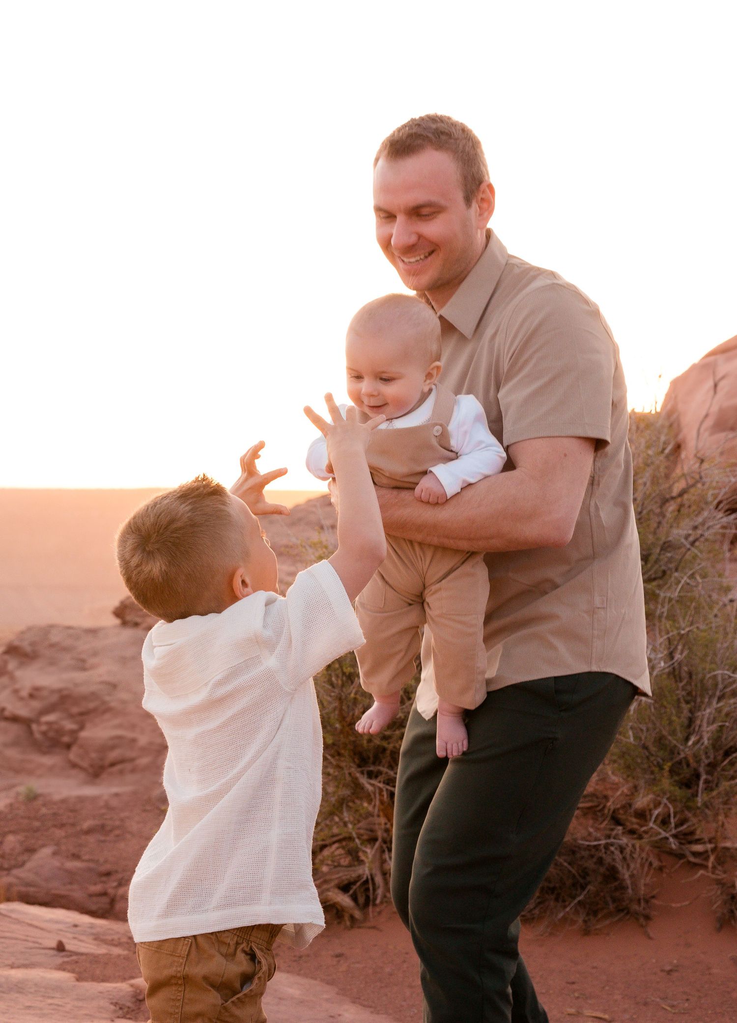 Joyful family interaction on red rocks during sunset with desert landscape in background.