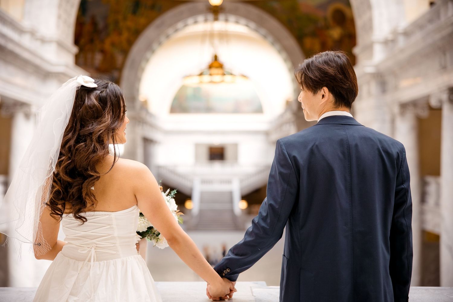 Wedding couple walking through an elegant marble hallway with classical architecture.