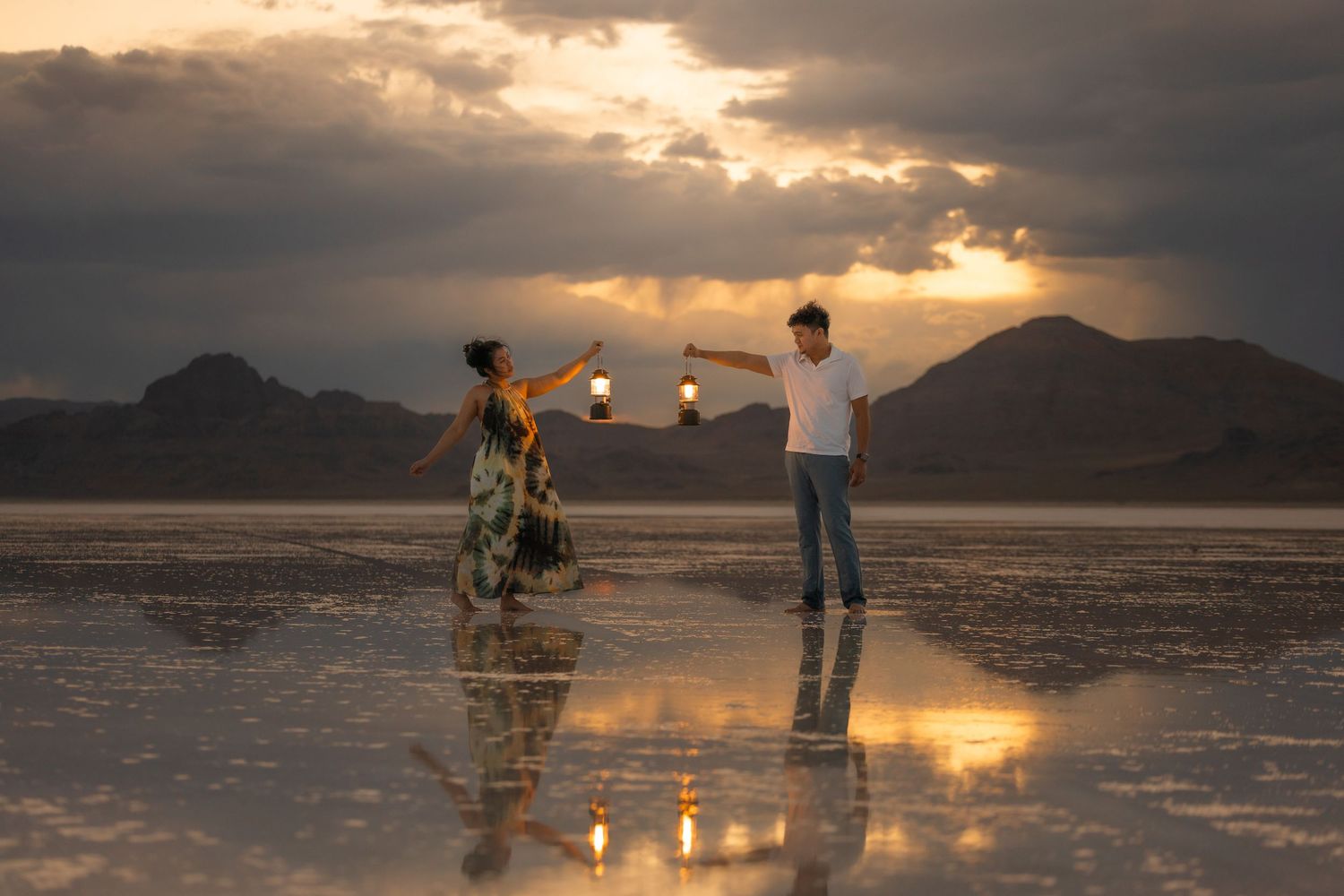 Two figures photographed at sunset on reflective water with dramatic mountain backdrop.