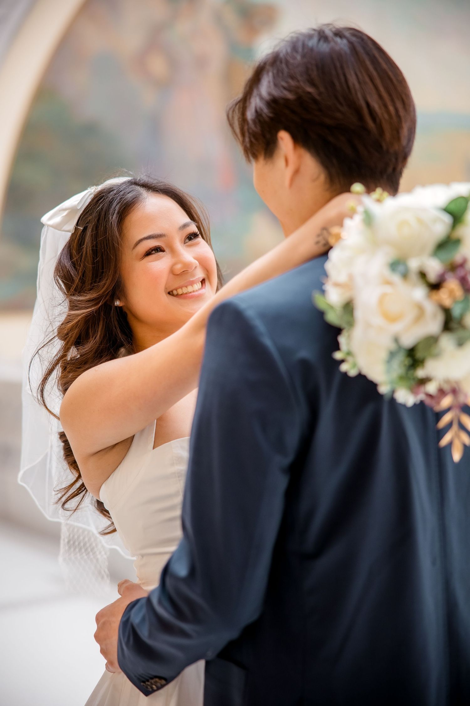 Couple embraces during romantic wedding photoshoot in soft natural lighting.