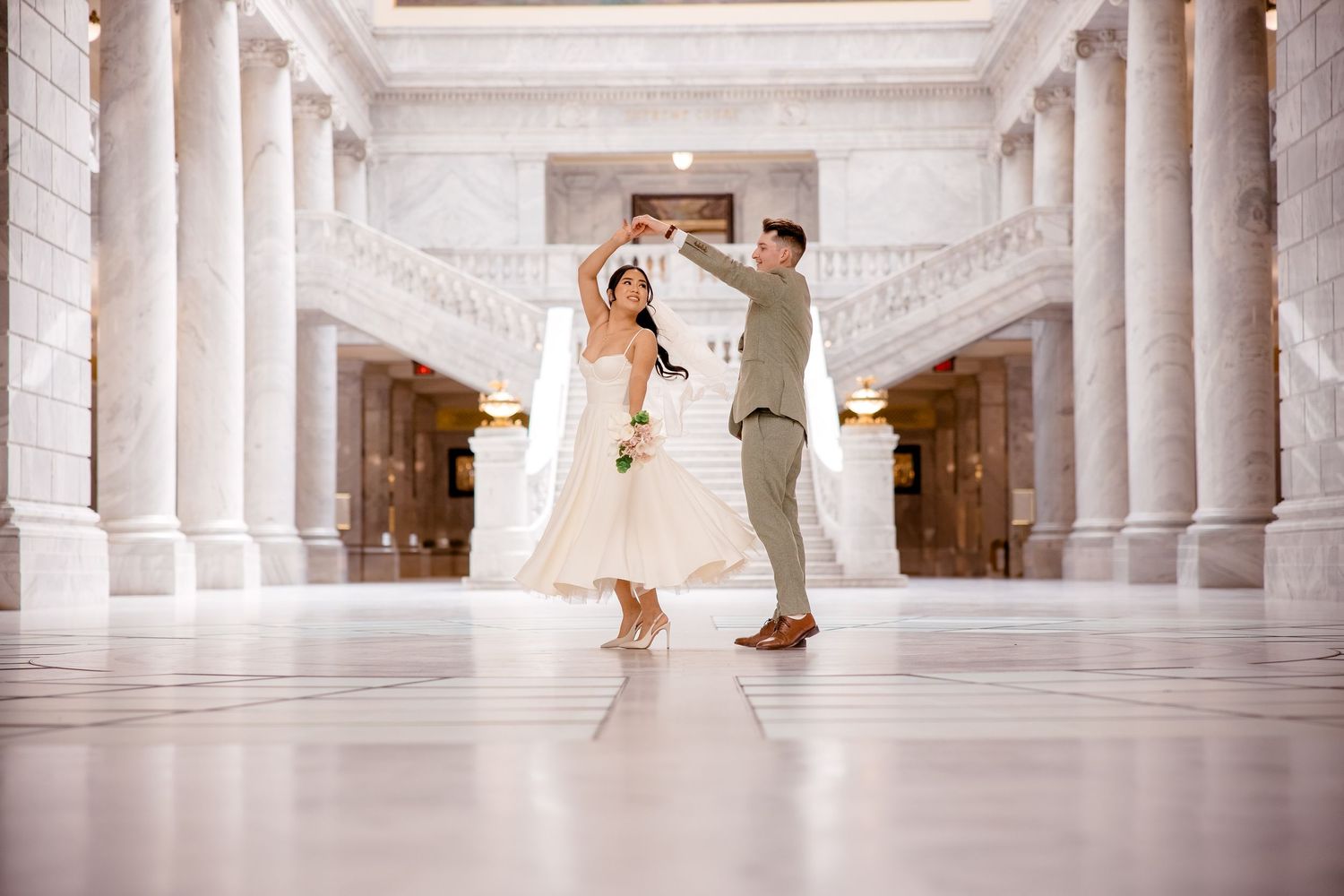 A wedding couple photographed in a grand white columned hallway.