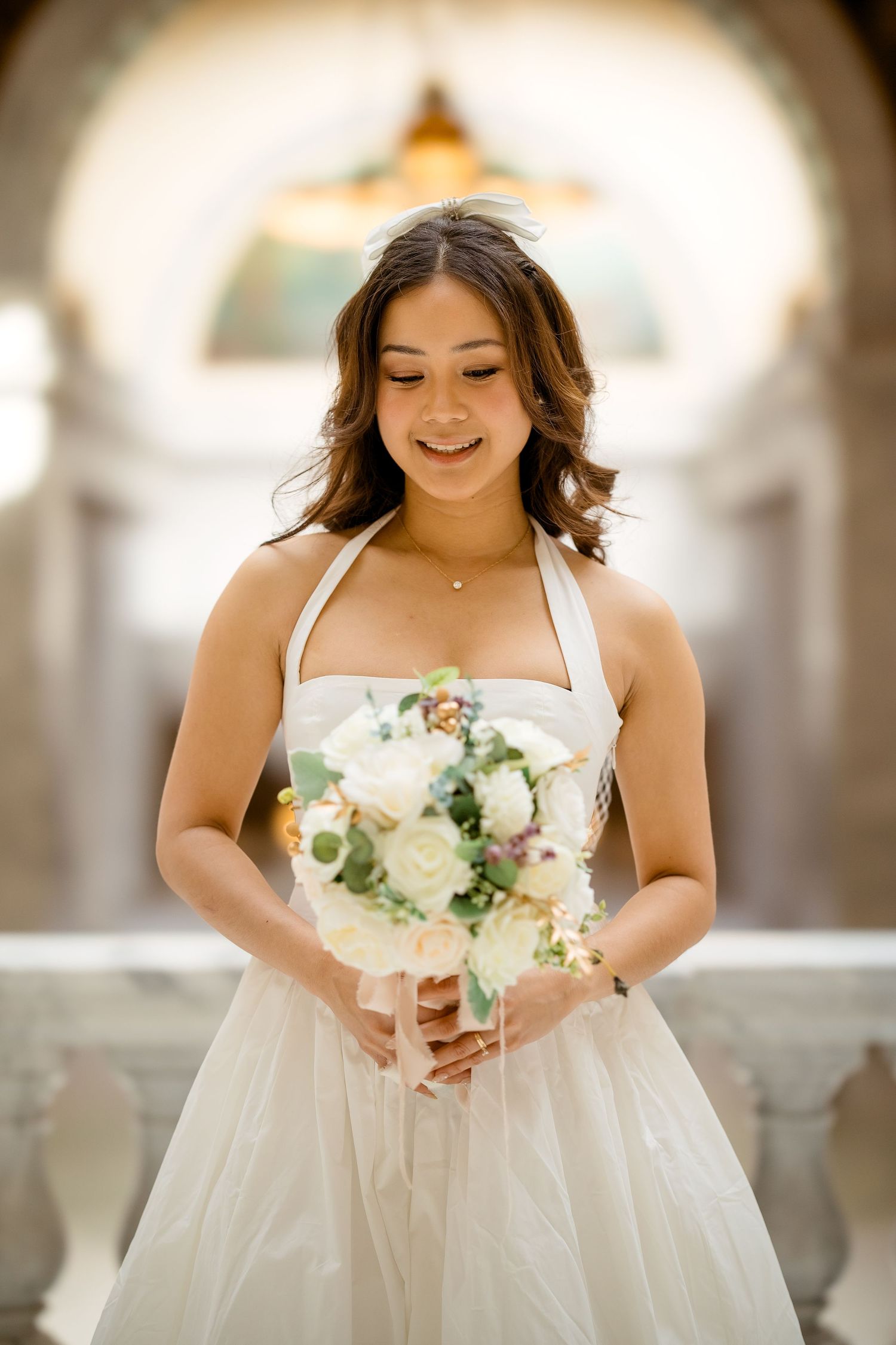 A bride in a white dress holding a beautiful bouquet of white roses and greenery.
