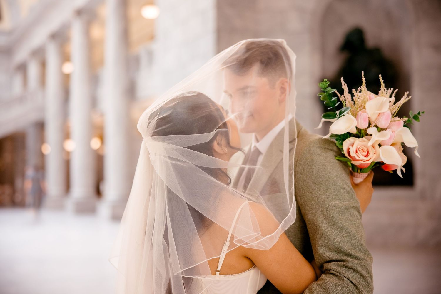 Tender wedding moment photographed in soft focus with flowing veil detail.