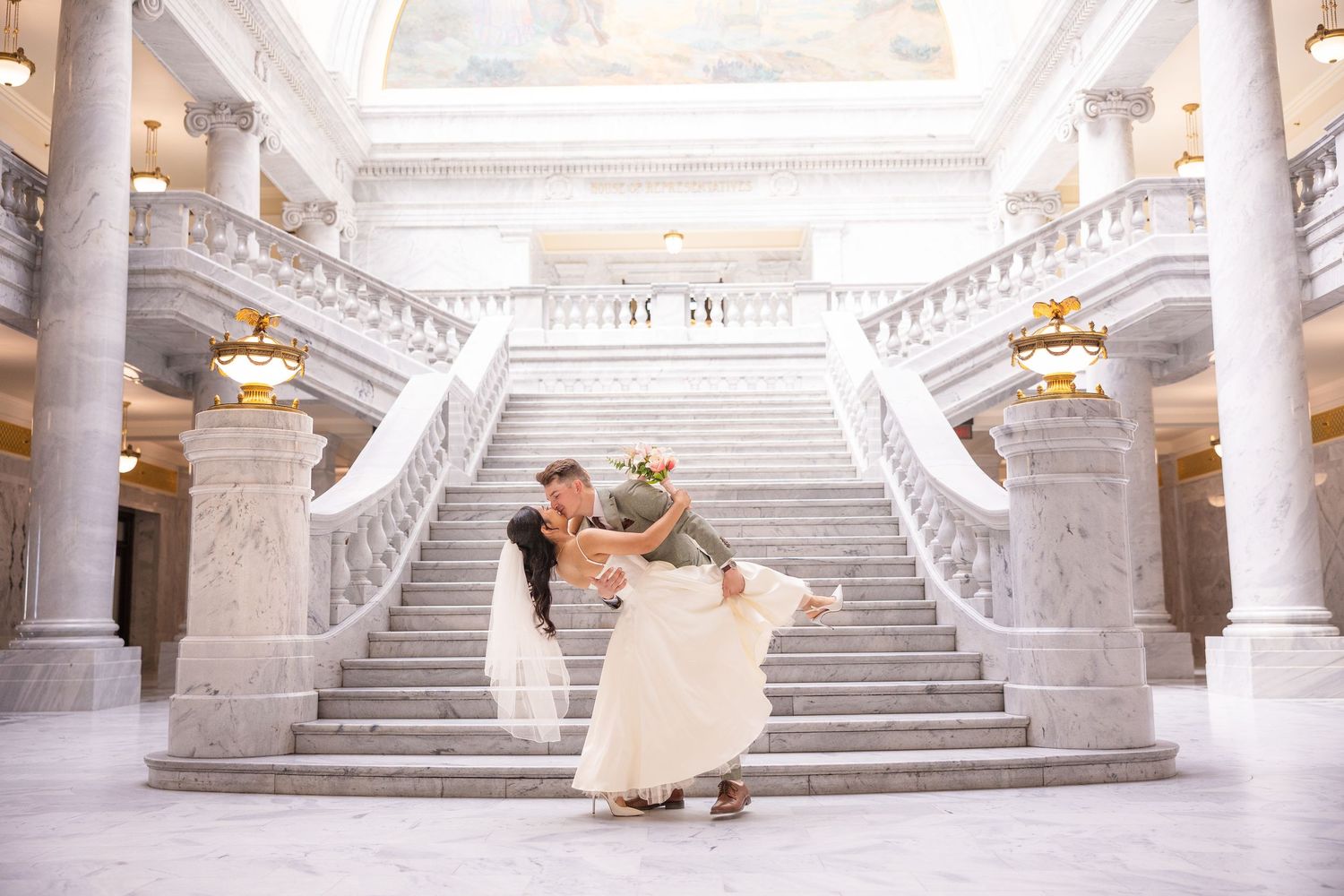 Elegant wedding couple poses on grand marble staircase with classical columns.