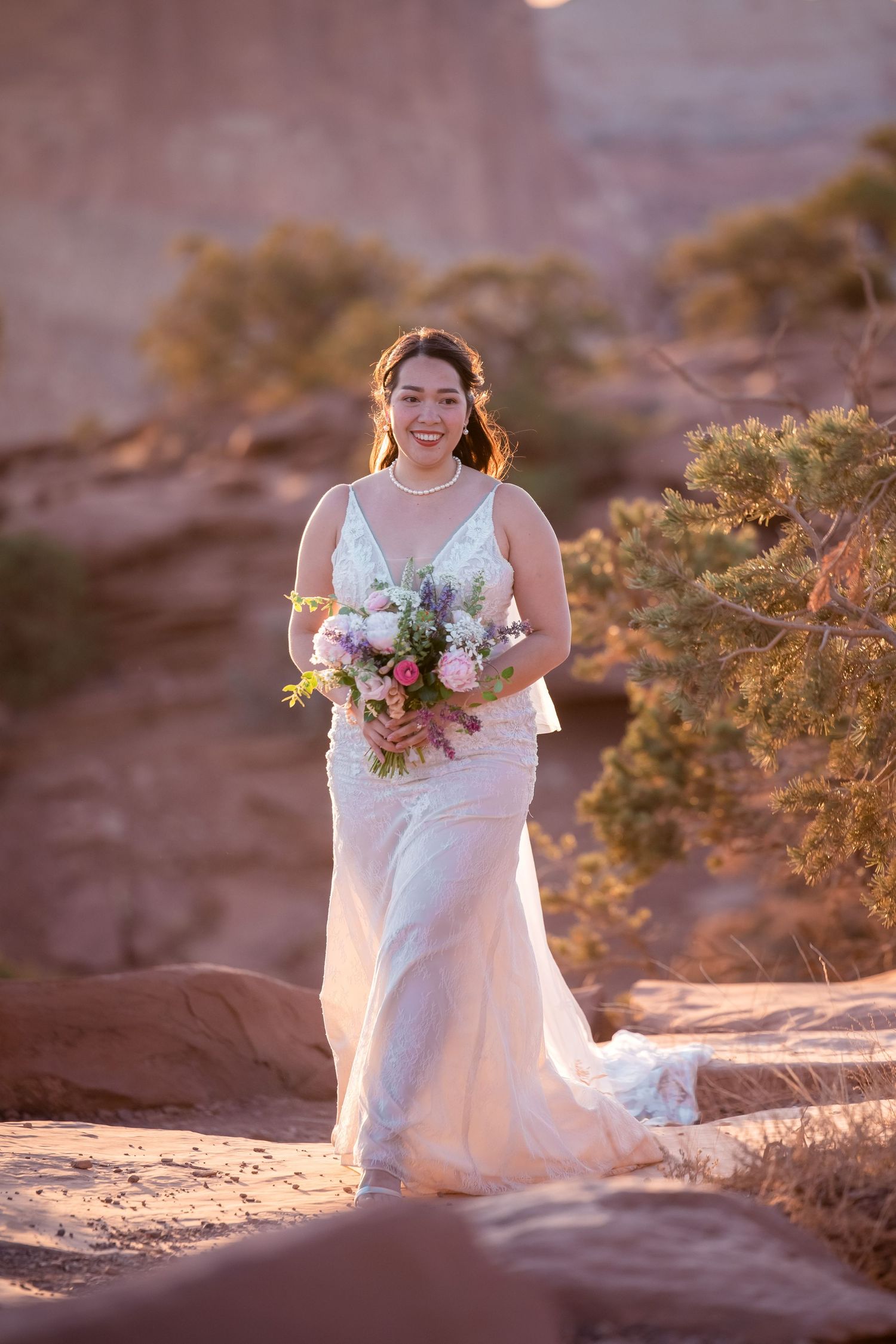 A bride in a white dress holds a colorful bouquet against a desert backdrop.