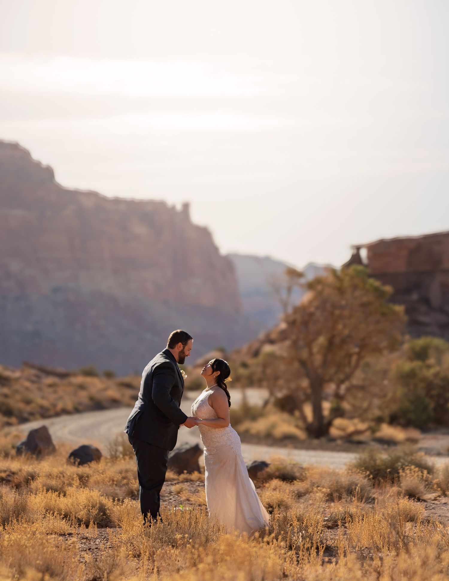 Couple walks through desert brush with dramatic canyon walls in the background.