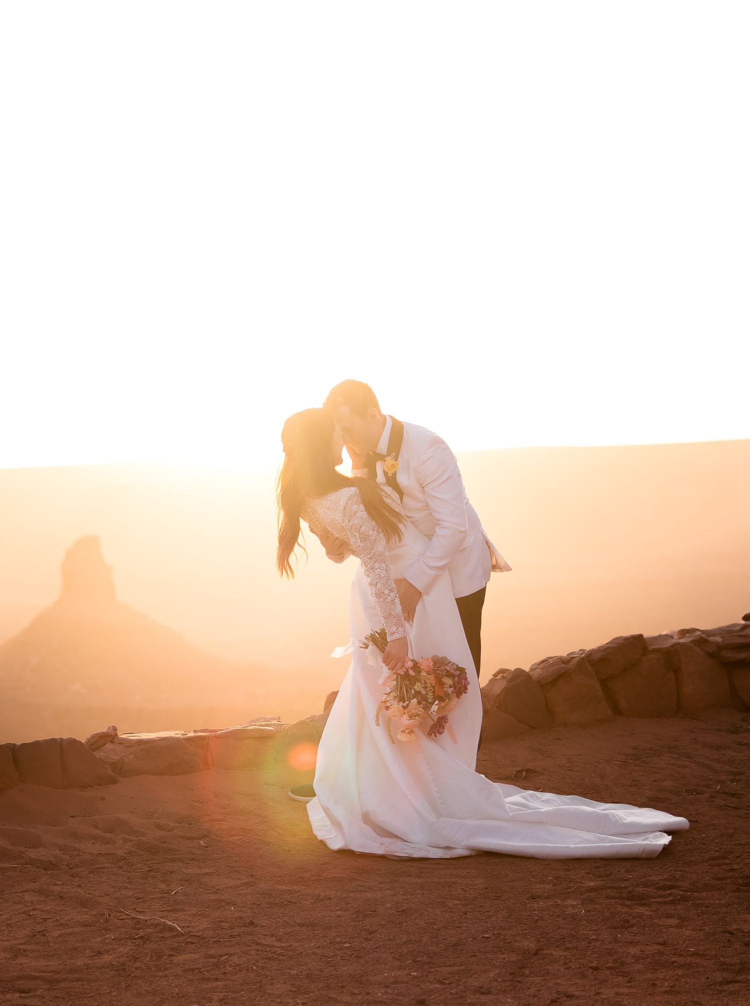 A silhouetted wedding couple embracing during golden hour in a desert setting.