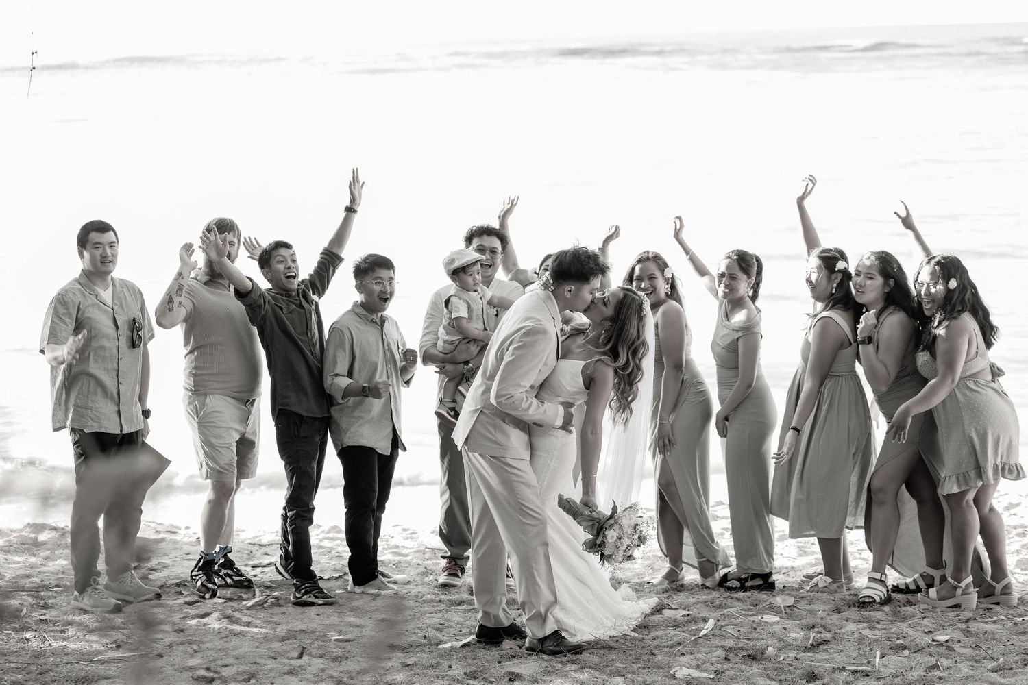 A joyful wedding celebration on the beach with a group of people raising their hands in celebration.