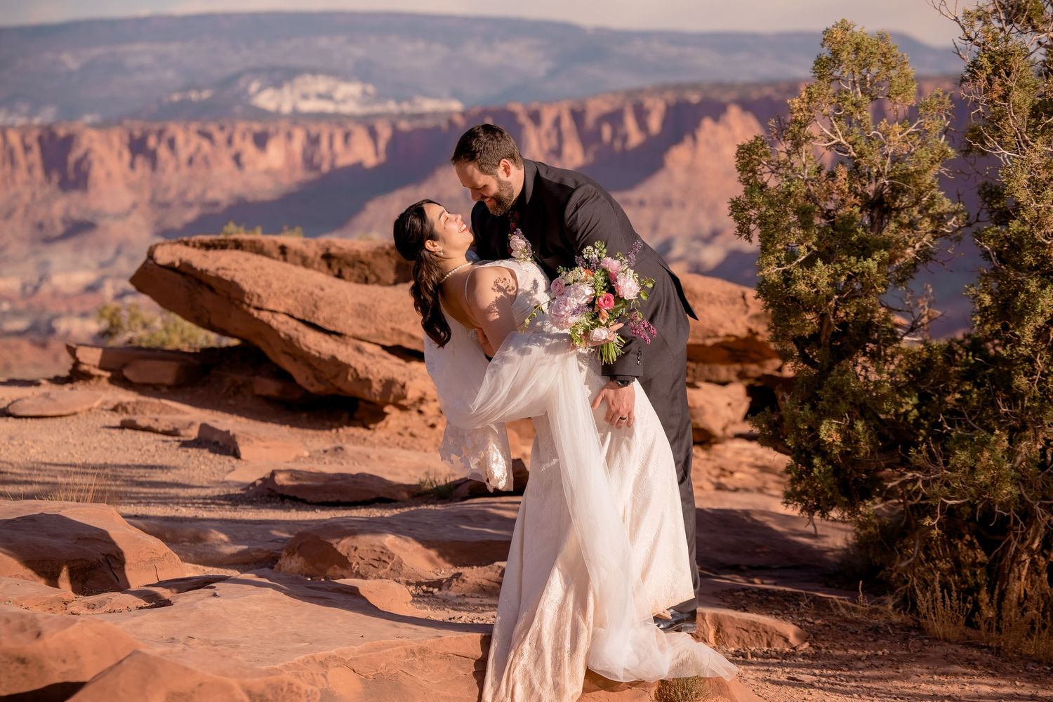 Wedding couple shares intimate moment against stunning red rock canyon backdrop.