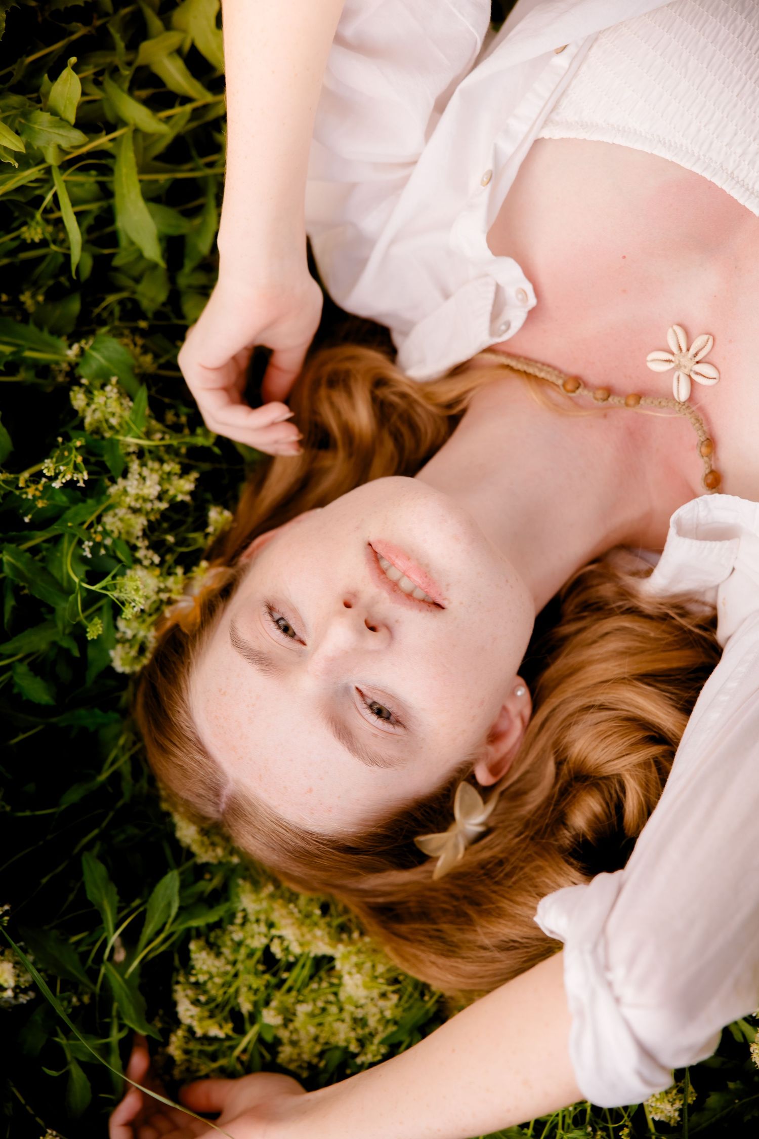 Dreamy portrait of someone lying in grass with white clothing and delicate floral accessories.