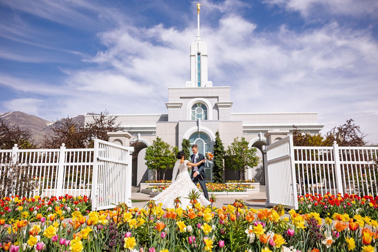White temple spires rise above colorful spring tulip gardens under a bright blue sky.