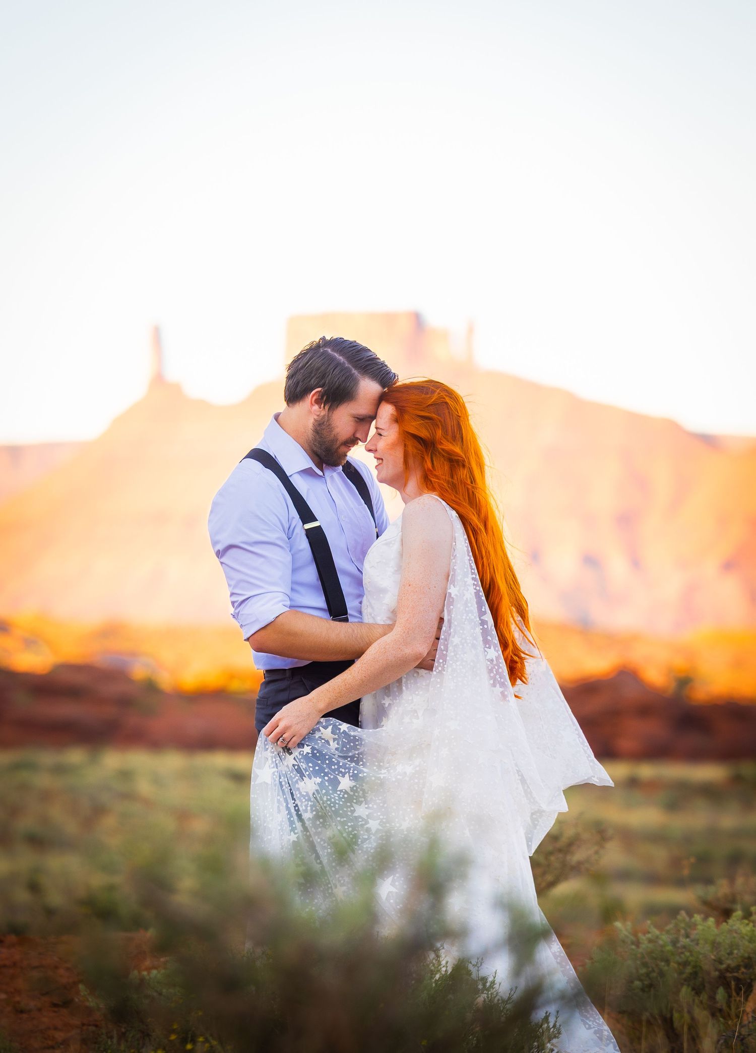 A romantic sunset photoshoot with a couple in wedding attire against a desert backdrop.