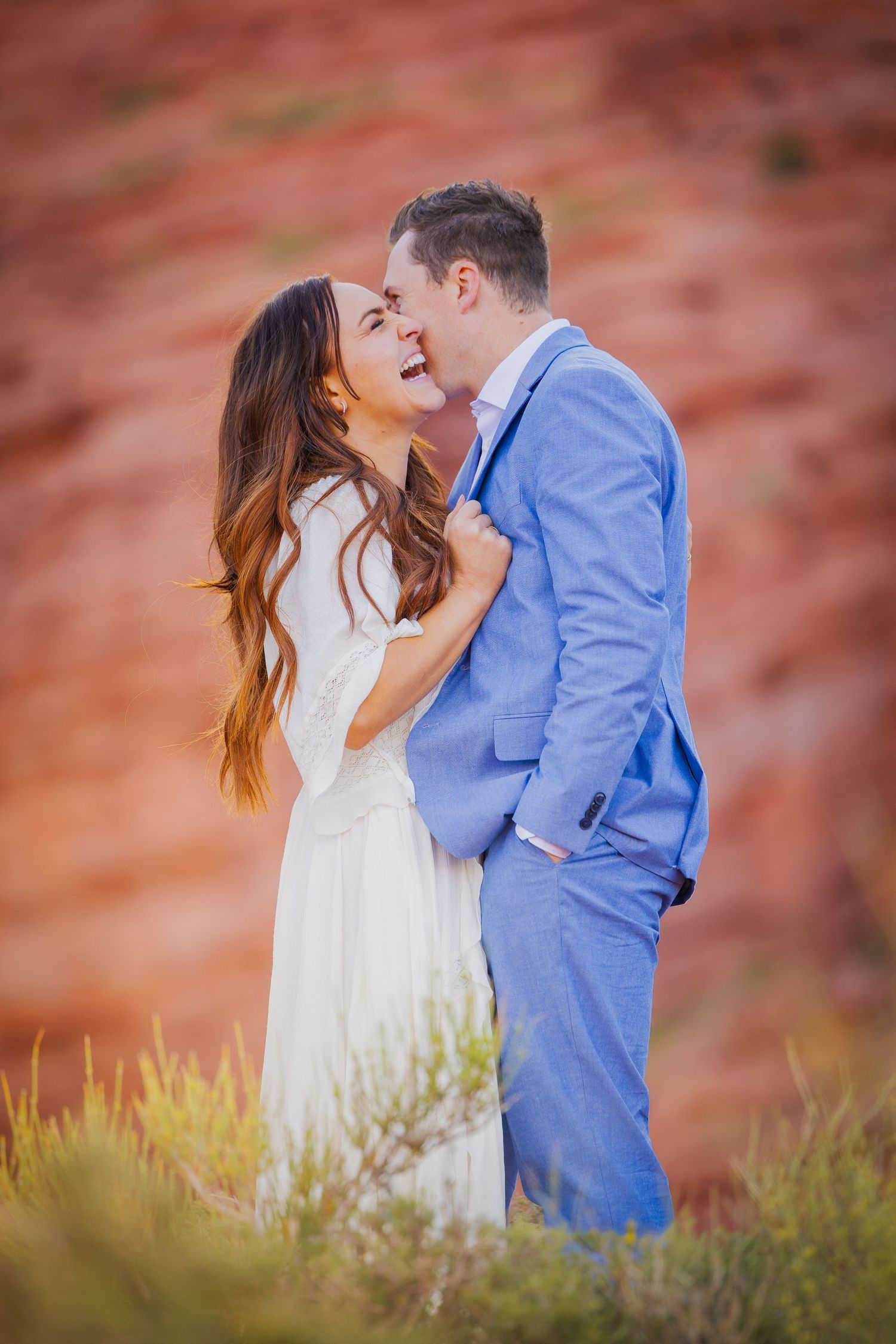 A tender moment between newlyweds against vibrant red rock cliffs.