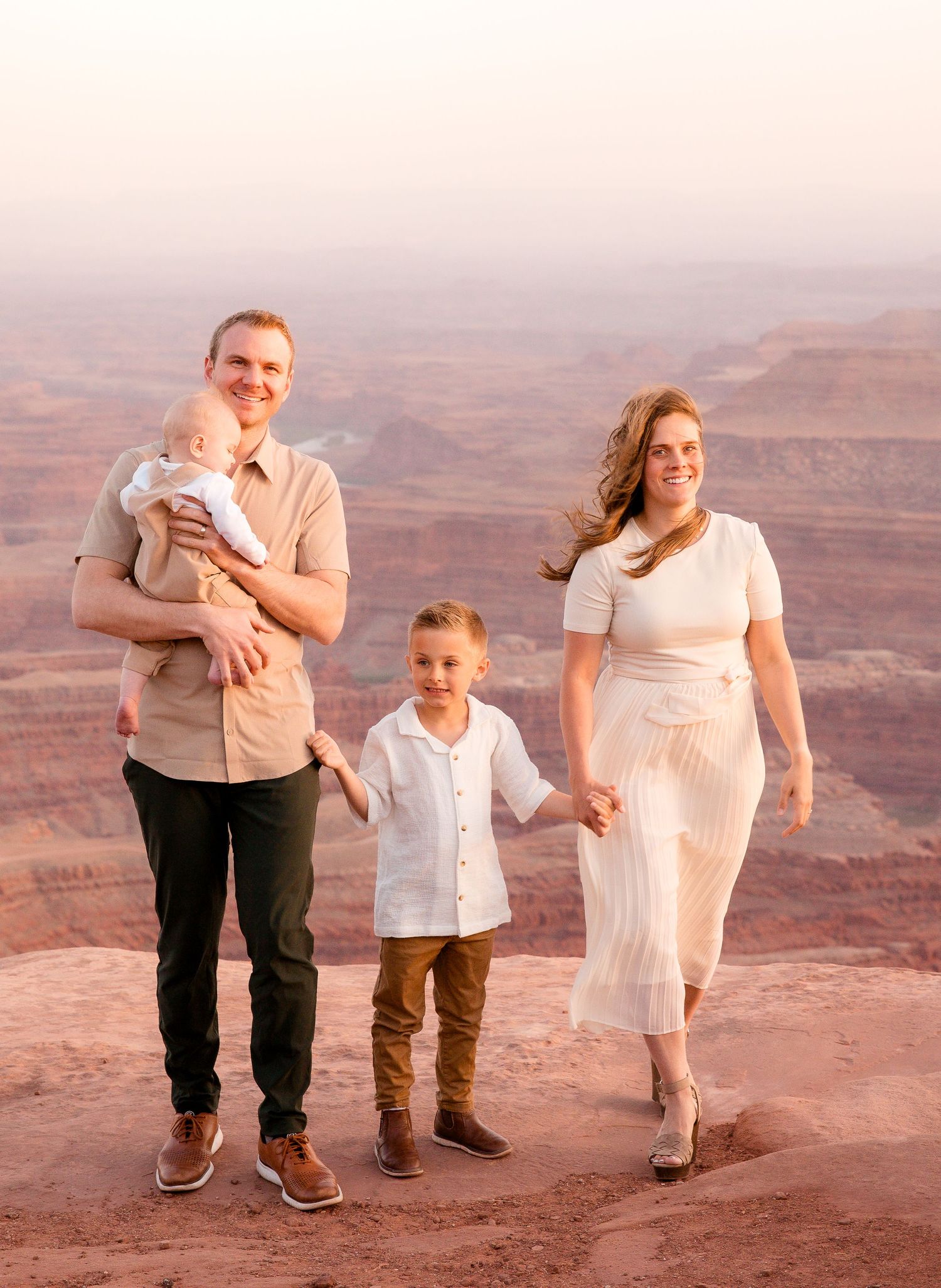 Family enjoying a sunset walk together on red rock cliffs overlooking a canyon vista.