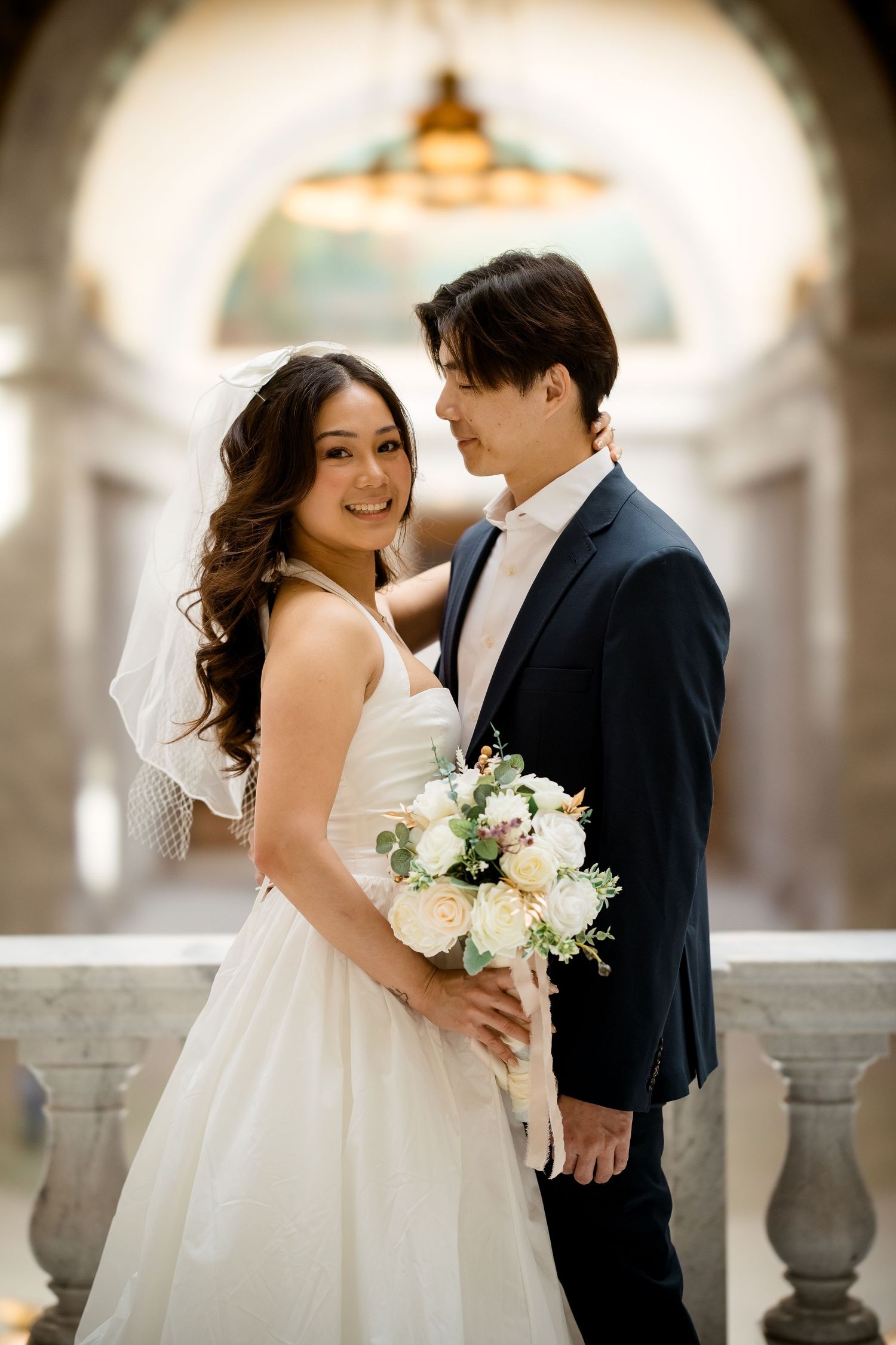 A romantic wedding photoshoot in an elegant columned venue with soft natural lighting.