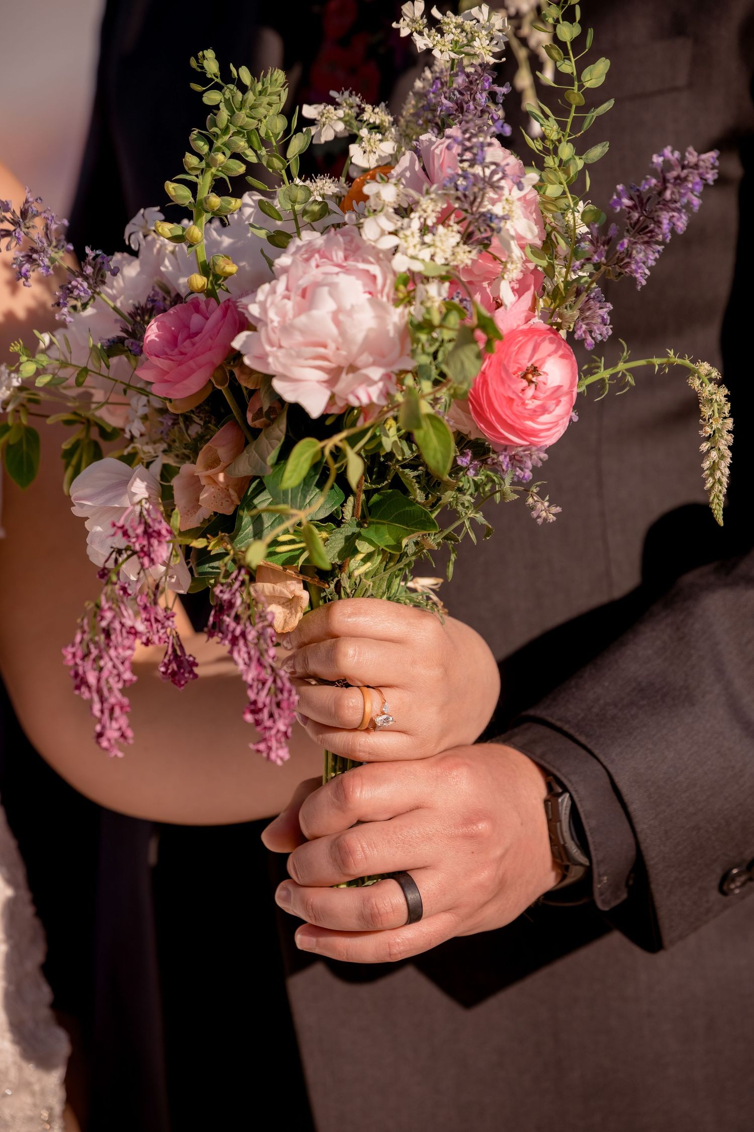 A beautiful bouquet with pink roses, lilacs, and greenery held in hands.
