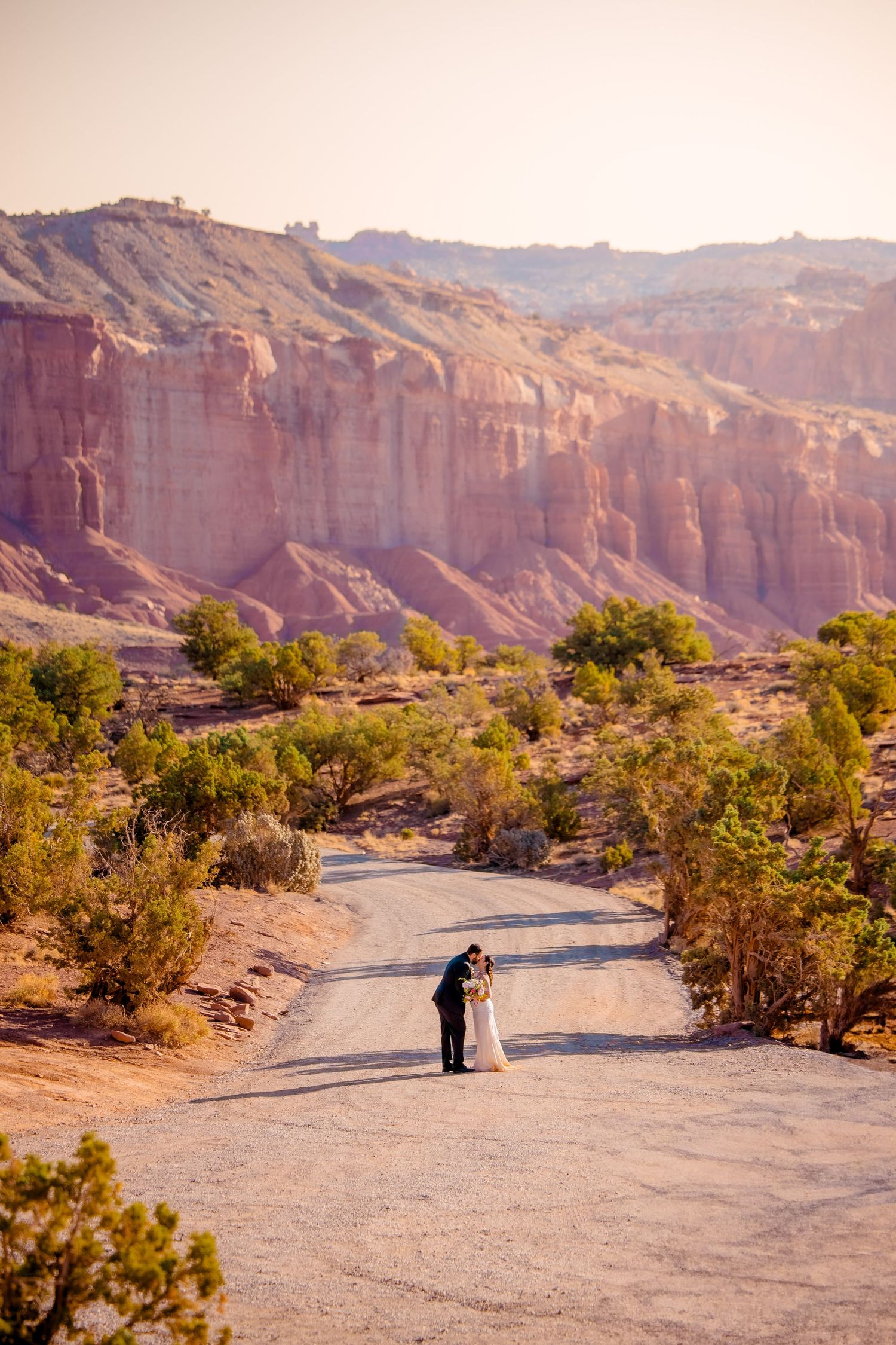 A wide landscape shot of a desert wedding with red rock cliffs and winding road.