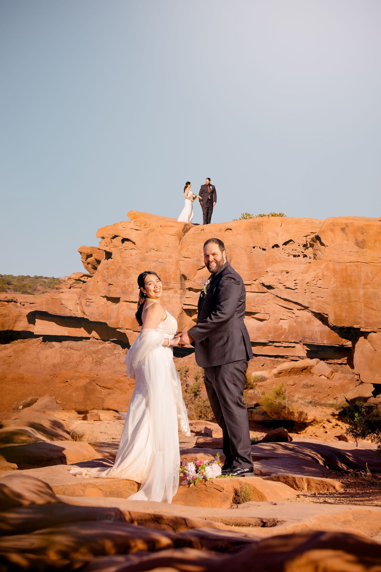 Wedding couple stands on dramatic red rock formations during outdoor ceremony.