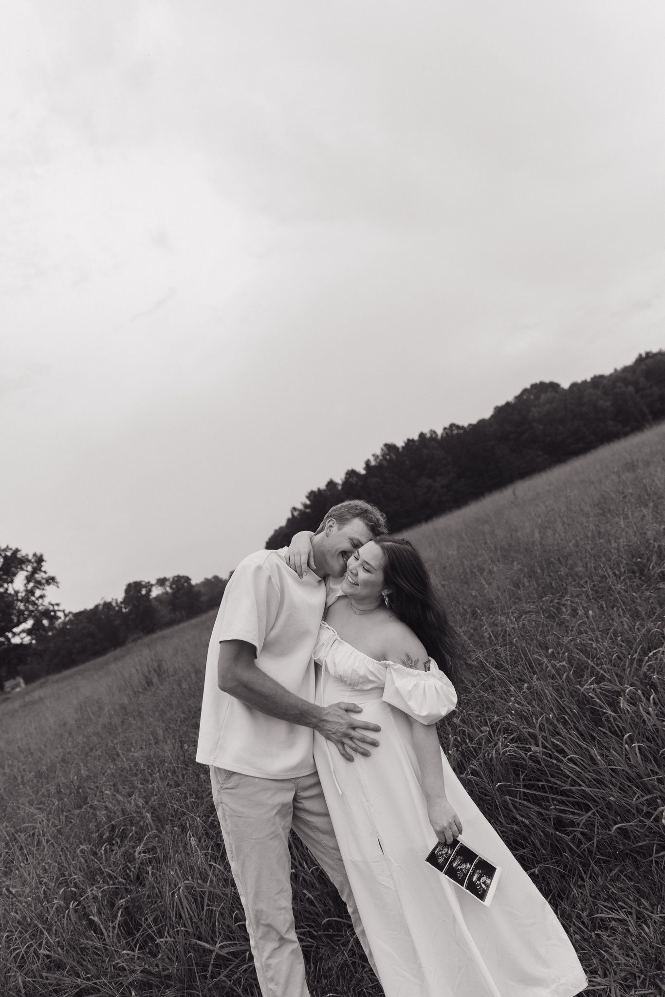 A romantic black and white photography series showing a couple embracing in a grassy field at sunset.