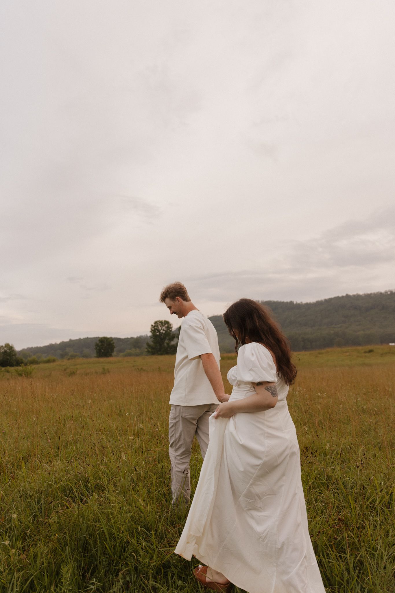 Couple shares tender moments together while dressed in flowing white outfits in a meadow landscape.
