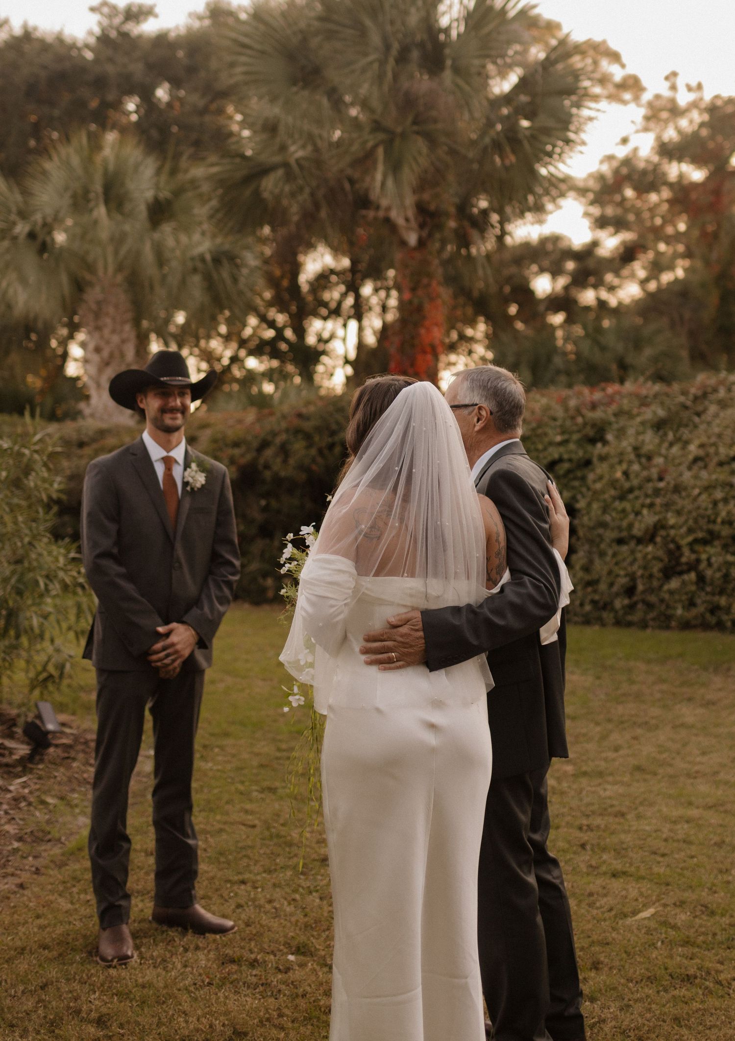 A romantic outdoor wedding ceremony unfolds at sunset with a couple and officiant surrounded by lush greenery.