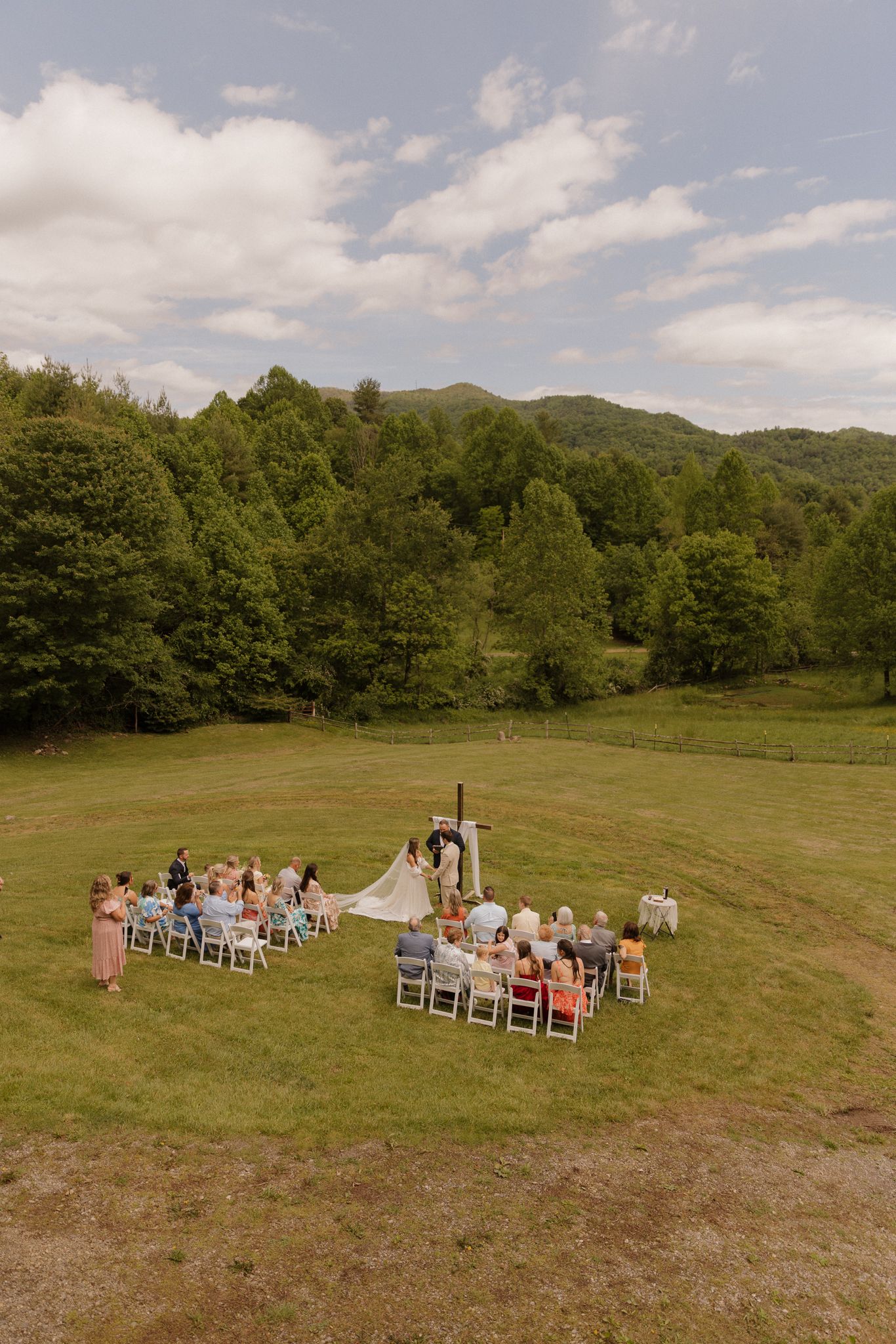 Outdoor mountain wedding ceremony setup with white chairs arranged on a grassy field.