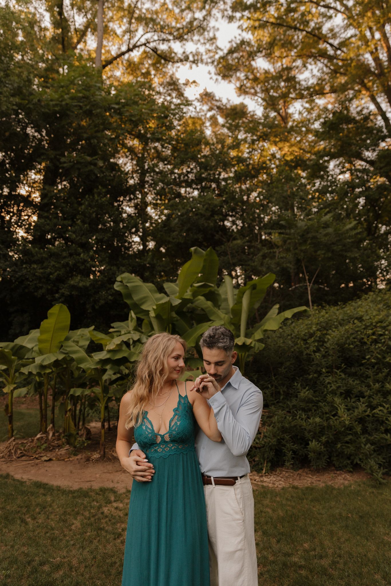 A couple shares a romantic moment in a garden setting with golden hour lighting and a teal dress.